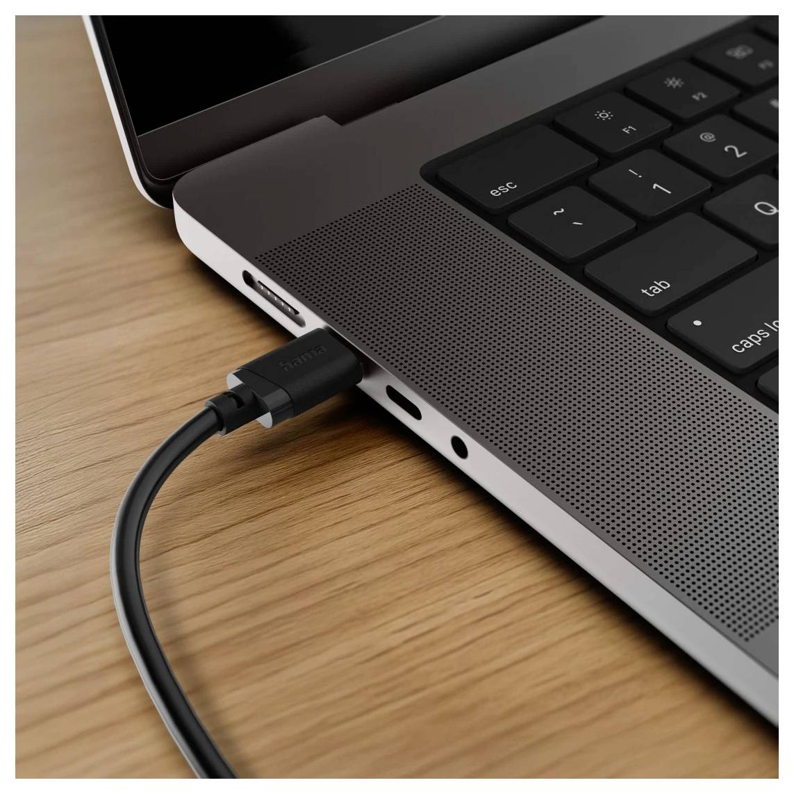 Detail snímku strany notebooku s připojeným USB-C kabelem na dřevěném stole.