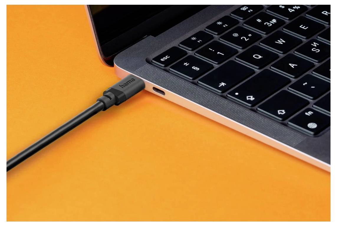 Detailní pohled na notebook s kabelem USB-C připojeným do bočního portu na oranžovém povrchu.