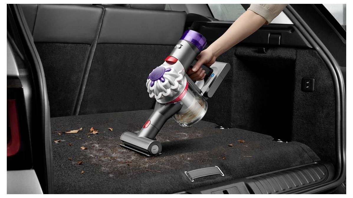 Ruční bezšňůrový vysavač čistí nečistoty a listí z koberce v kufru automobilu.