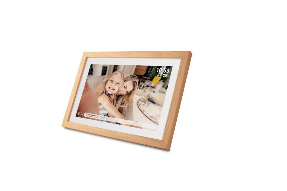 Dřevěný digitální fotorámečk zobrazující usmívající se ženu a dítě u stolu s časem 10:53 zobrazeným v rohu.