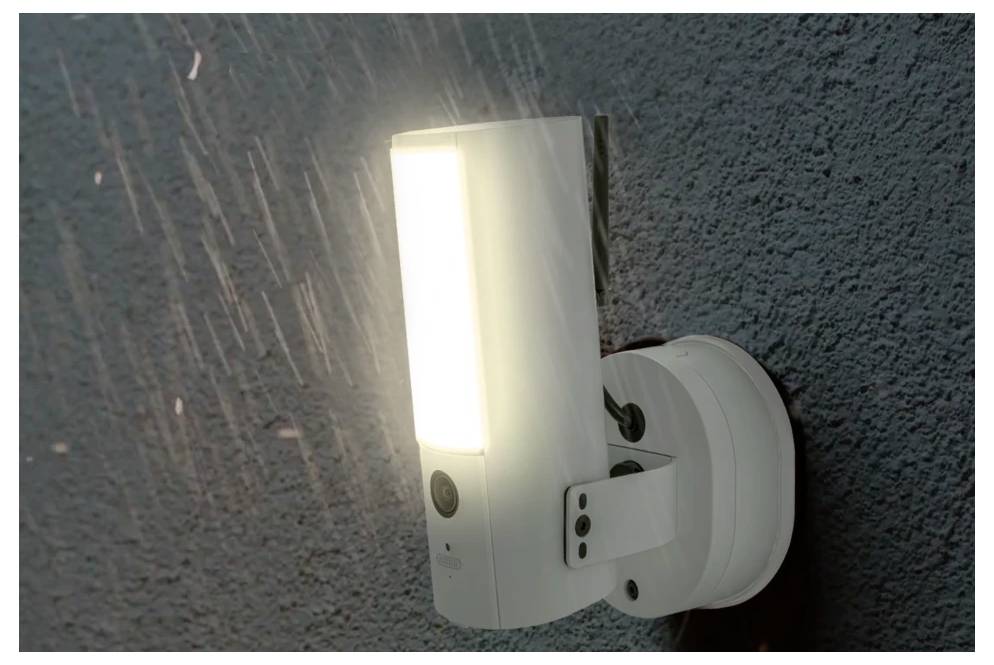 Bílé nástěnné LED osvětlení pro venkovní použití svítící na strukturované vnější zdi v noci.
