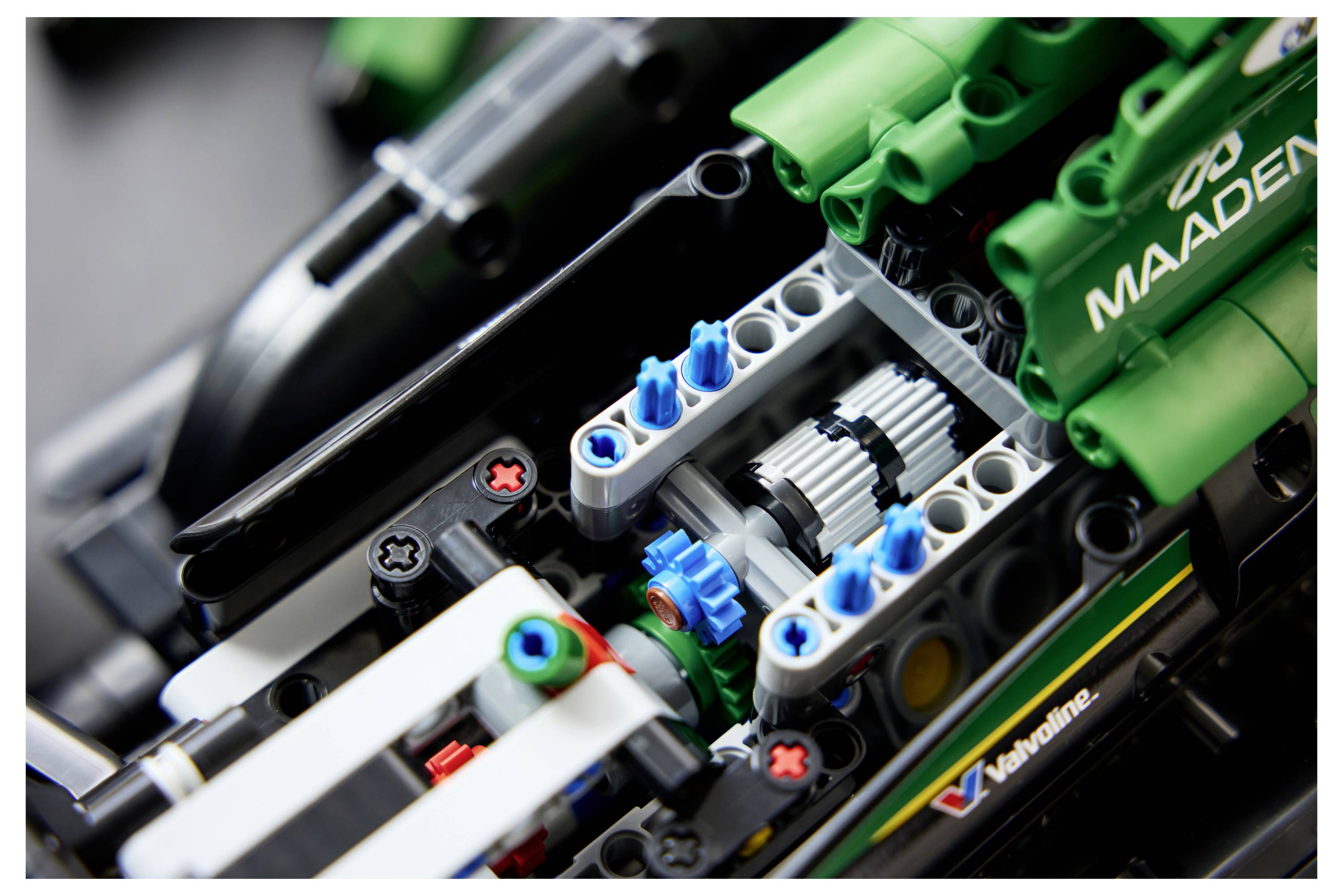 Detailní pohled na motor vozidla LEGO Technic s viditelnými modrými ozubenými koly a zelenou značkou 'MAADEN'.