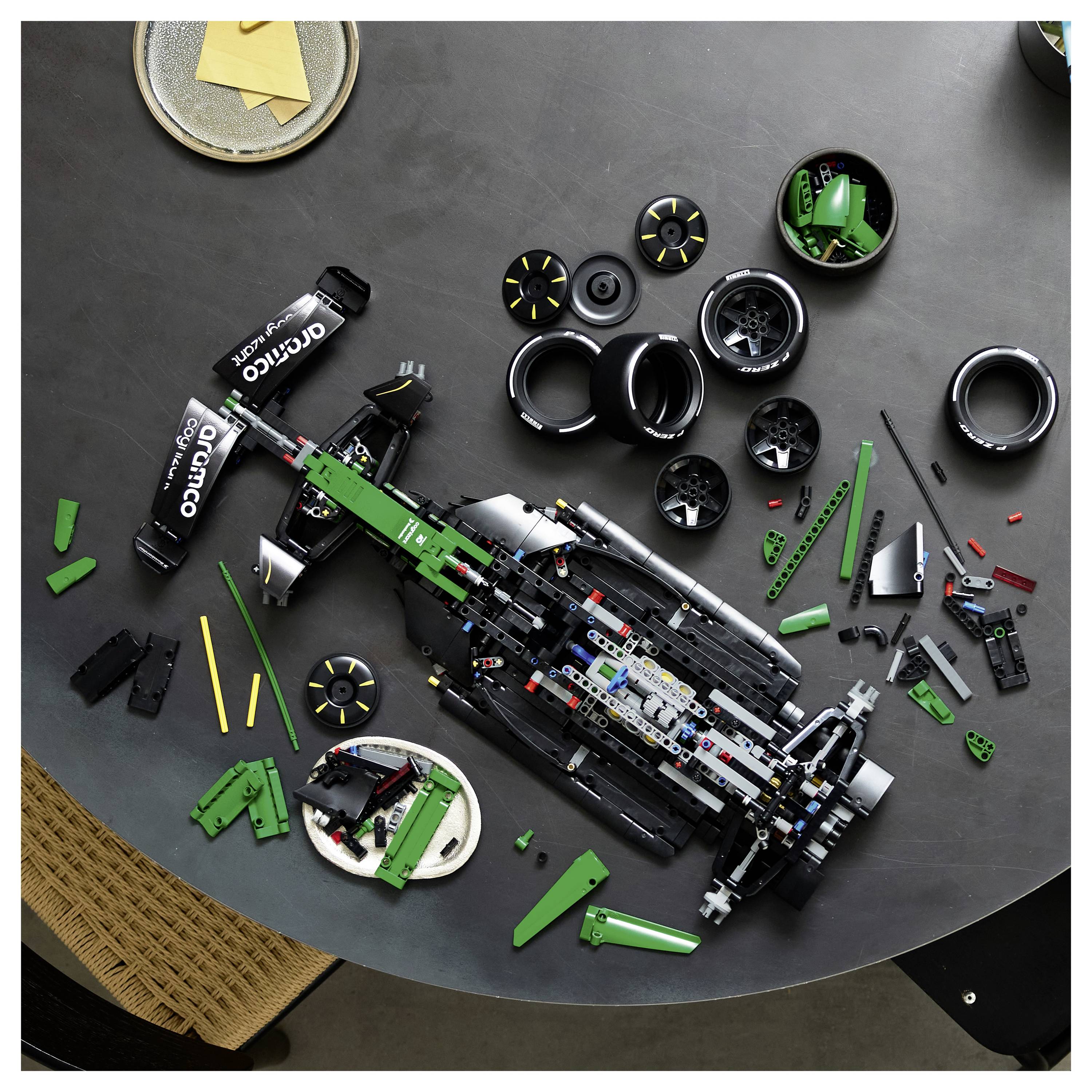 Pohled shora na částečně složené LEGO závodní auto Formule 1 s rozptýlenými koly a součástkami na stole.