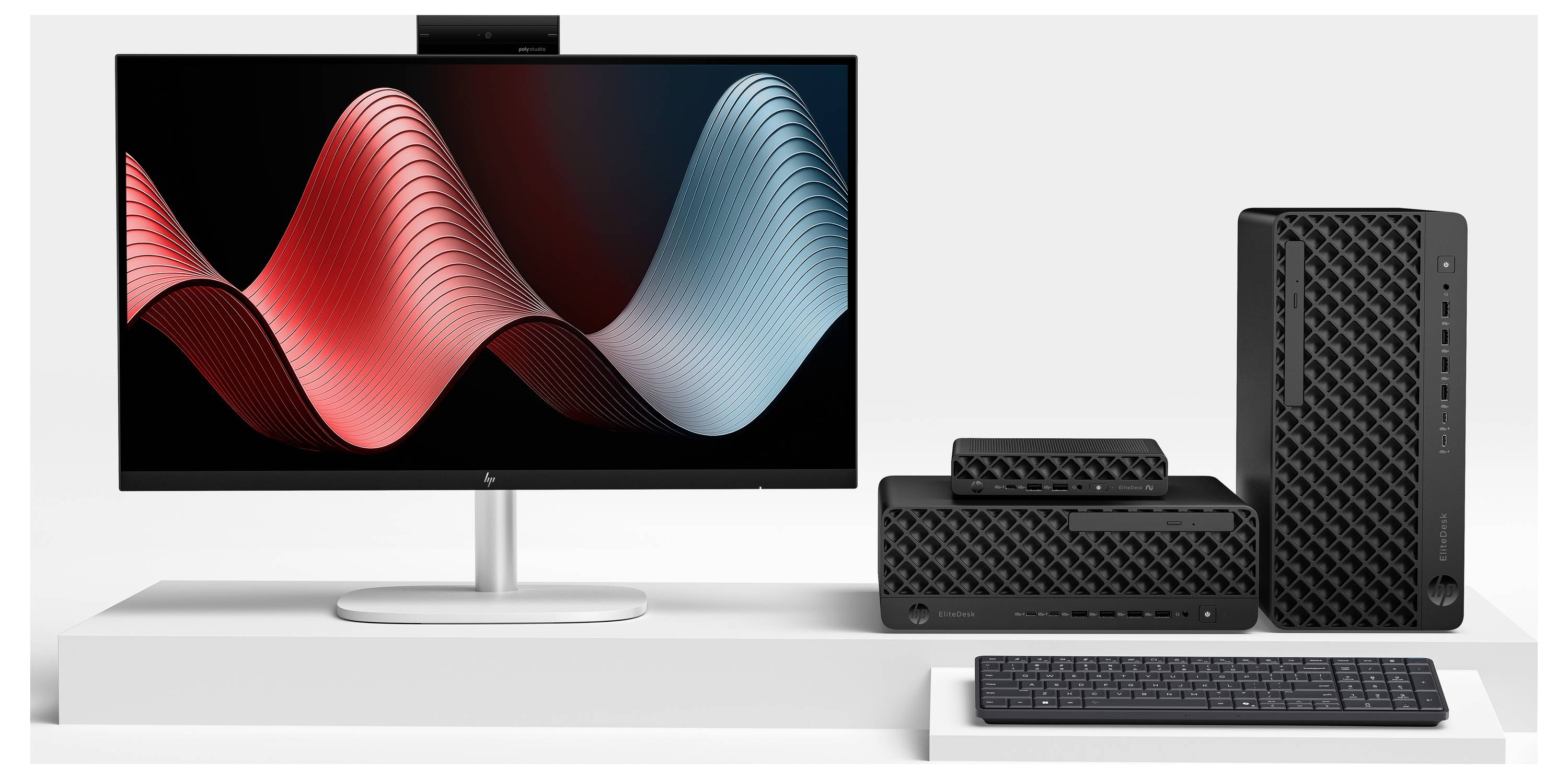 Nastavení stolního počítače se širokouhlým monitorem zobrazujícím abstraktní červené a modré vlnité grafiky, plus malá věž PC, reproduktor a klávesnice na bílém stole.