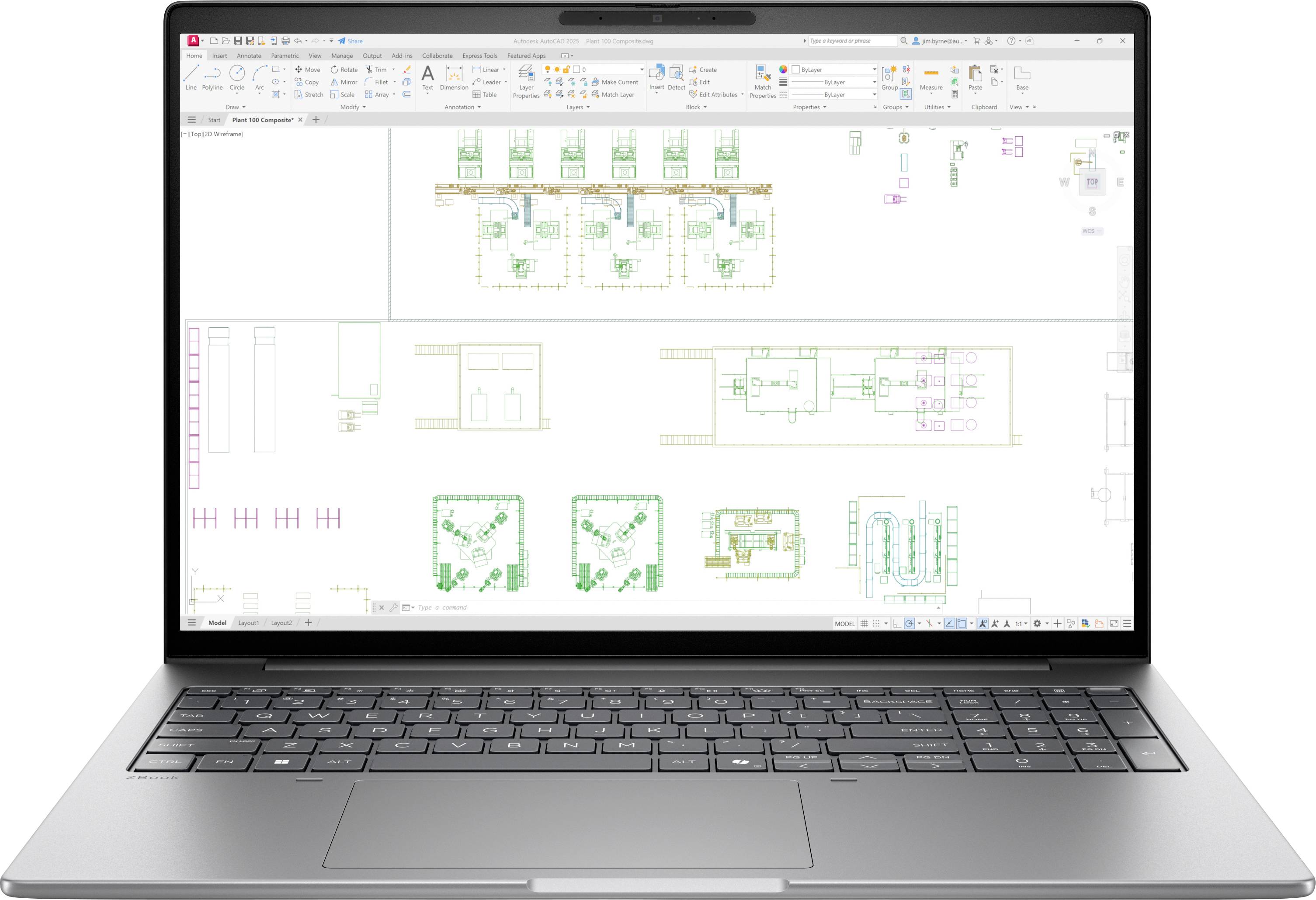 Přenosný počítač zobrazující CAD výkres plánu podlahy s více diagramy rozvržení budovy a barevnými technickými výkresy na bílém pracovním prostoru.