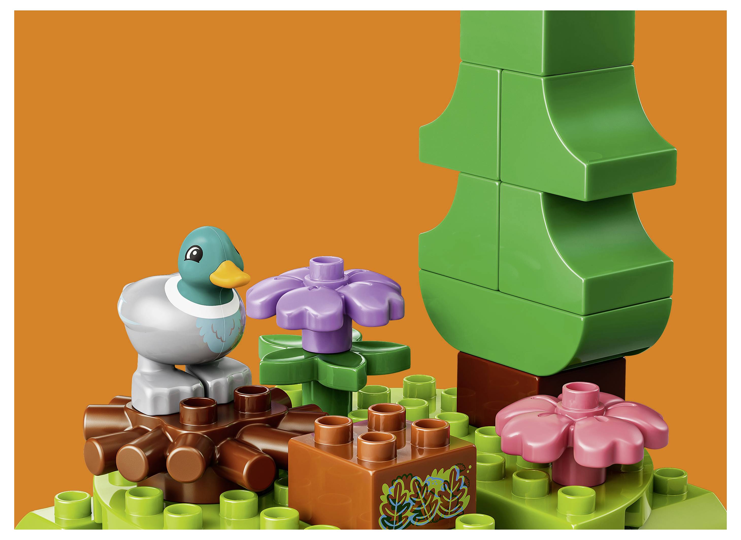 Pestrobarevná scéna ve stylu LEGO s kachnou, květinami a velkým zeleným stromem na oranžovém pozadí.