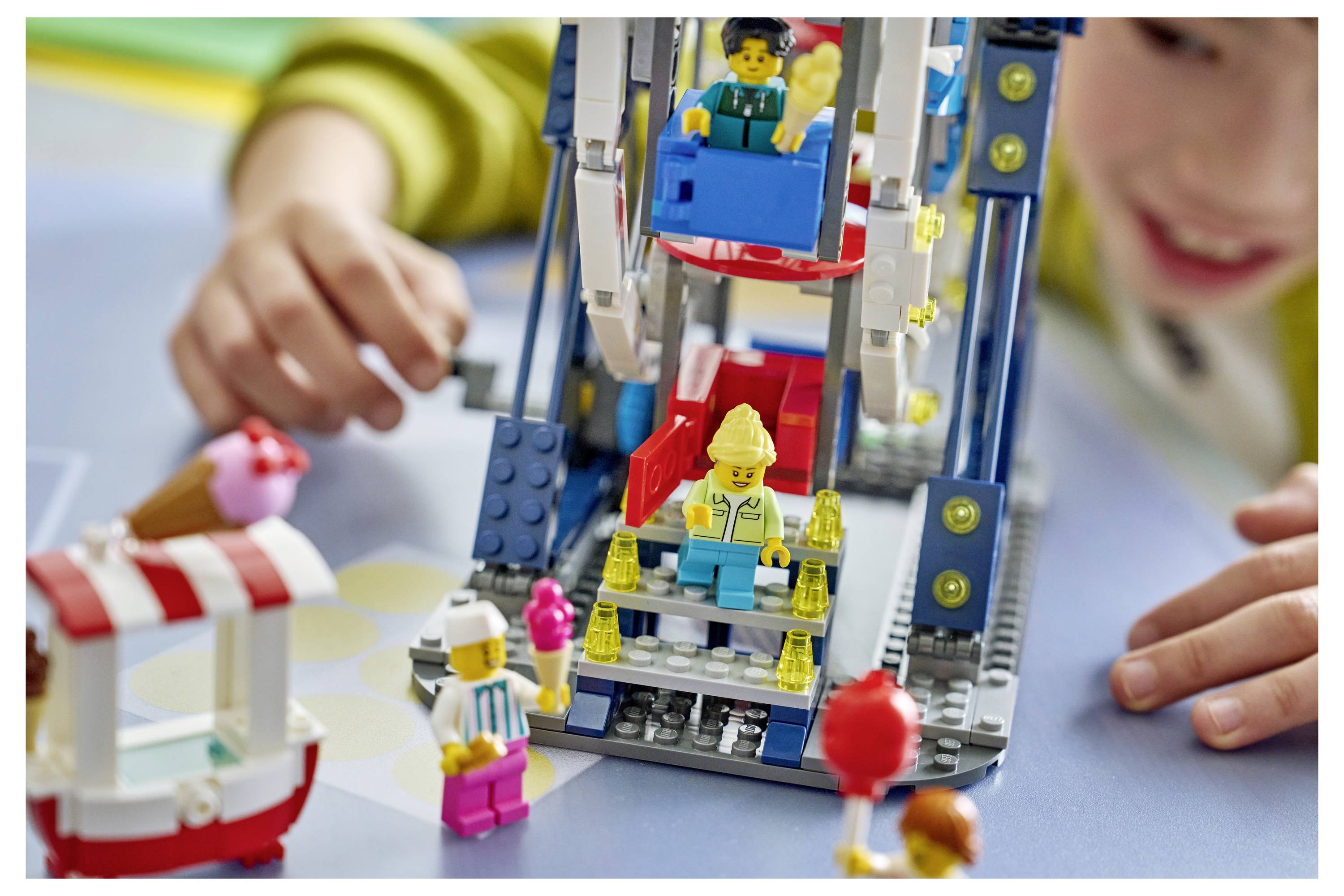 Dítě si hraje s barevnou LEGO atrakční jízdou nebo ruským kolem s několika miniaturními figurkami viditelnými na hravé scéně v interiéru.