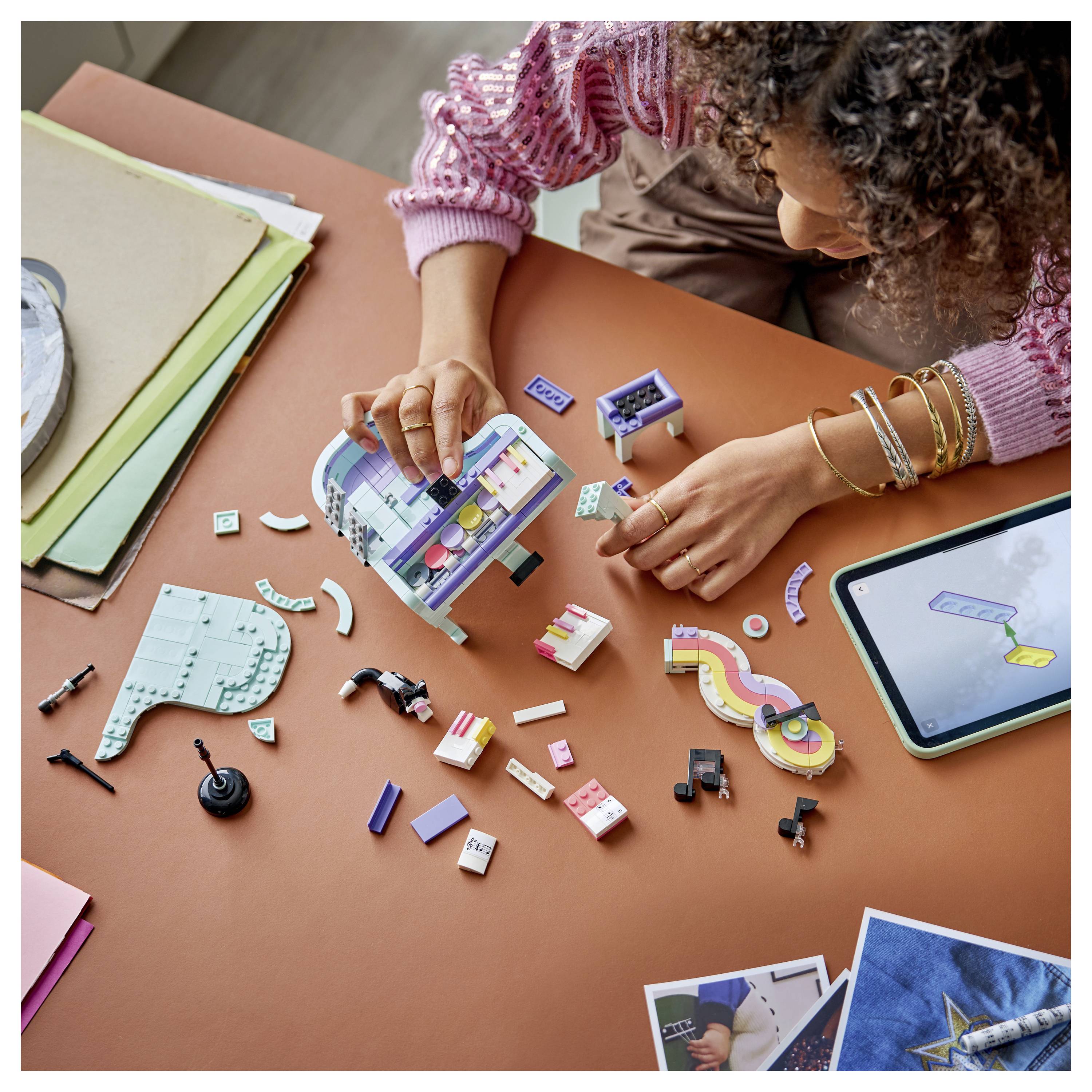 Osoba skládá barevný miniaturní stavební projekt v LEGO stylu u stolu, poblíž jsou volné díly, pokyny a tablet.