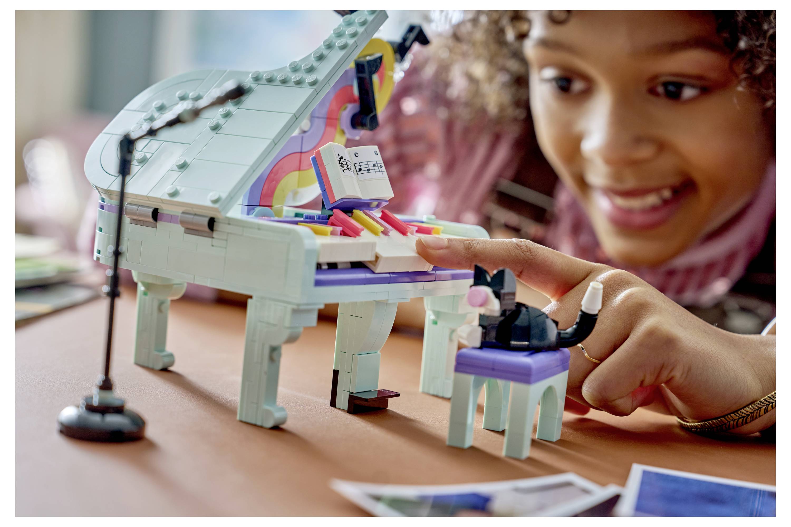 Dítě si hraje se sadou LEGO-podobného hračkového piana, stiskuje klávesy a usměje se na model na stole.