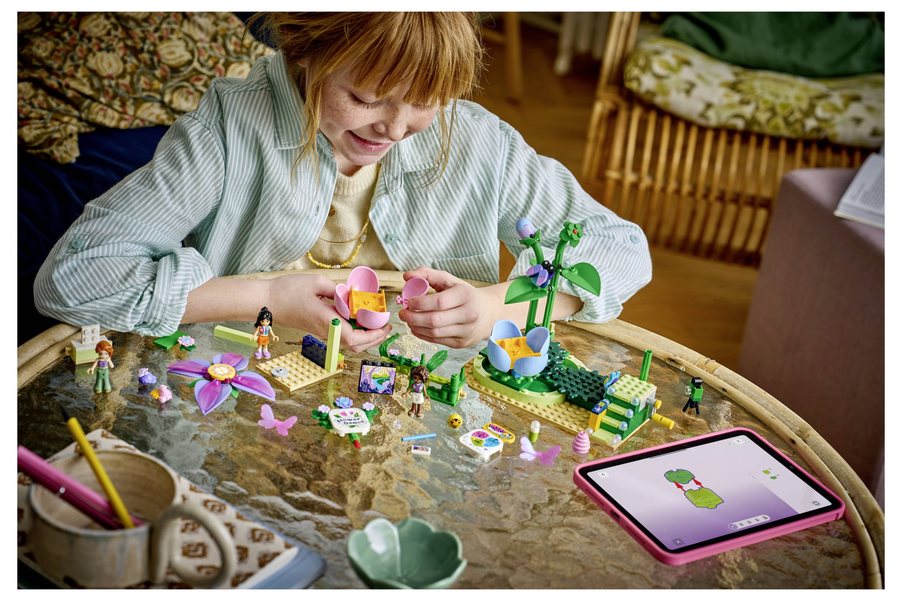 Dívka stavěící barevný LEGO květ v zahradě u stolu, poblíž tabletu, který zobrazuje průvodce modelem květiny.