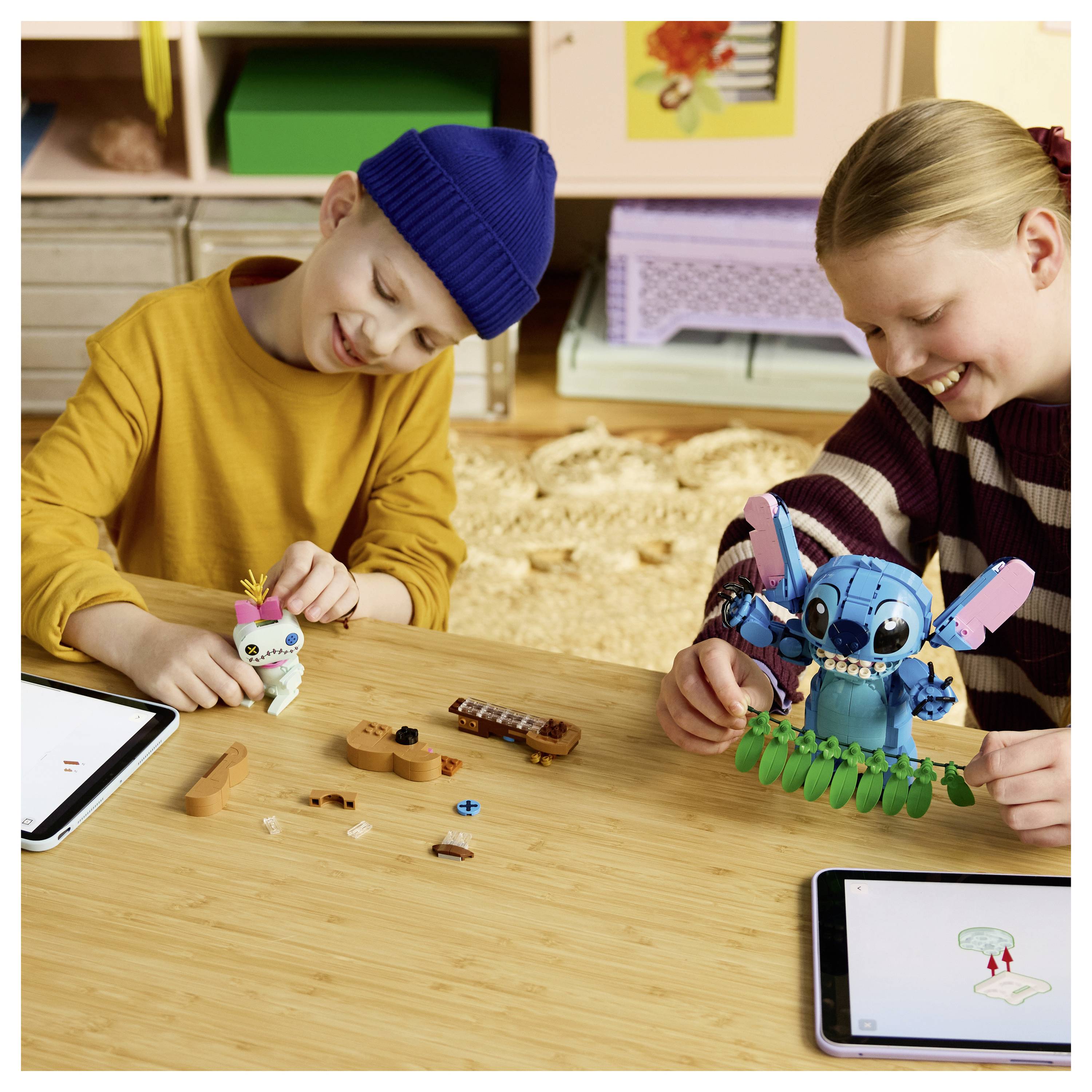 Dvě děti staví malé hračkové roboty u stolu, poblíž kterého jsou tablety se zobrazovanými instrukcemi.