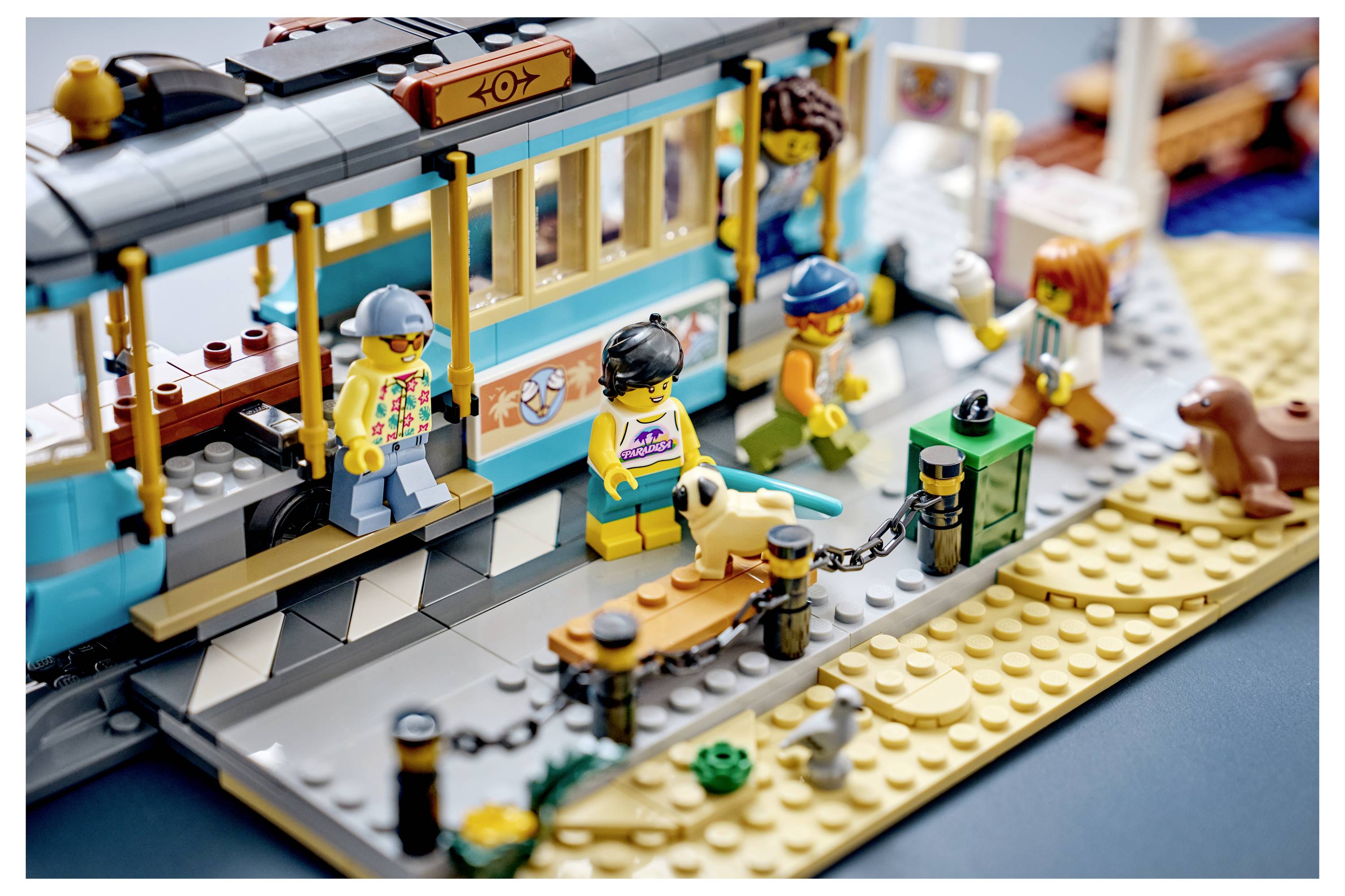 Scéna LEGO pláže s tramvají s cestujícími nastupujícími, včetně psa na písku poblíž zastávky.