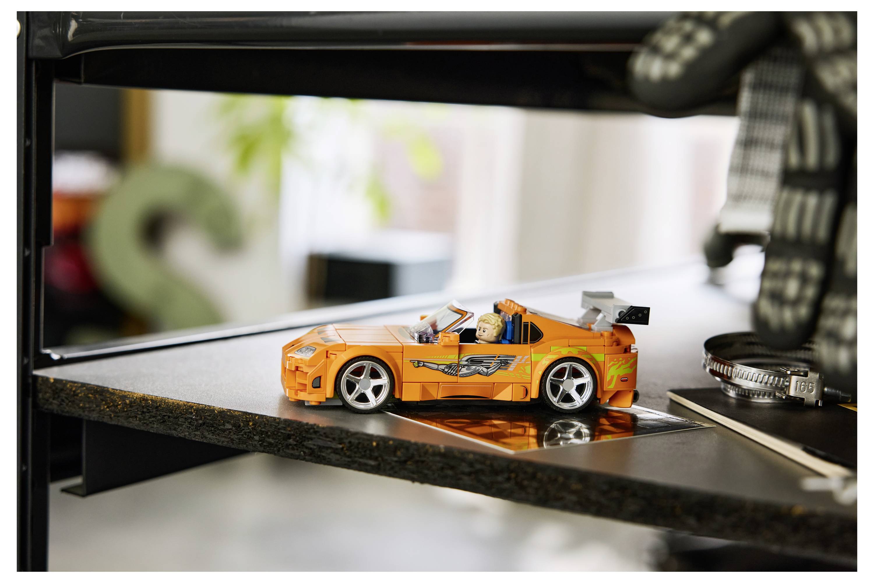 Oranžové hračkářské sportovní auto na reflexní tiskové desce 3D tiskárny s viditelným rámem tiskárny v pozadí.