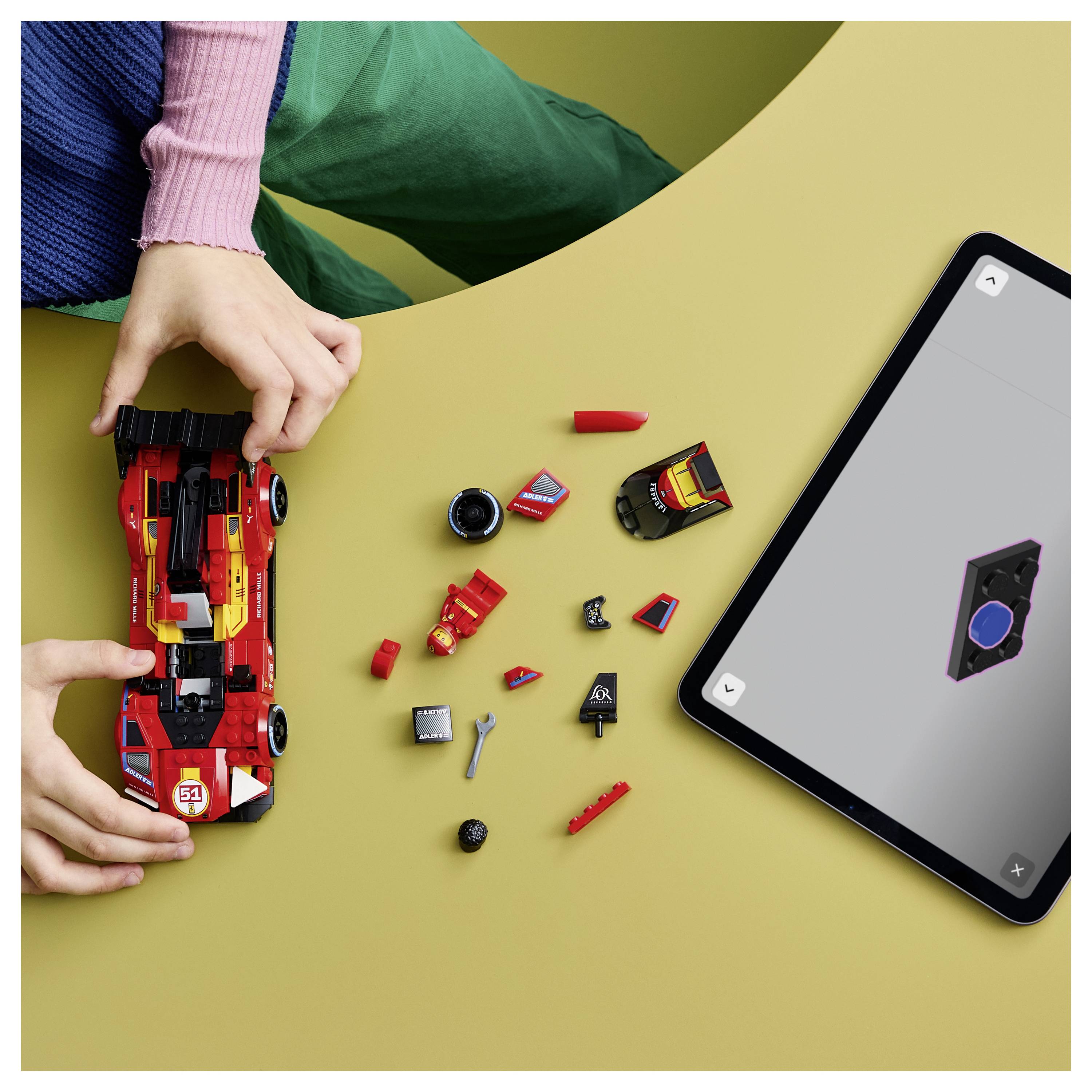 Dítě skládající červený hračkářský závodní vůz z LEGO-podobných dílků vedle tabletu zobrazujícího design vozu na žluté ploše.