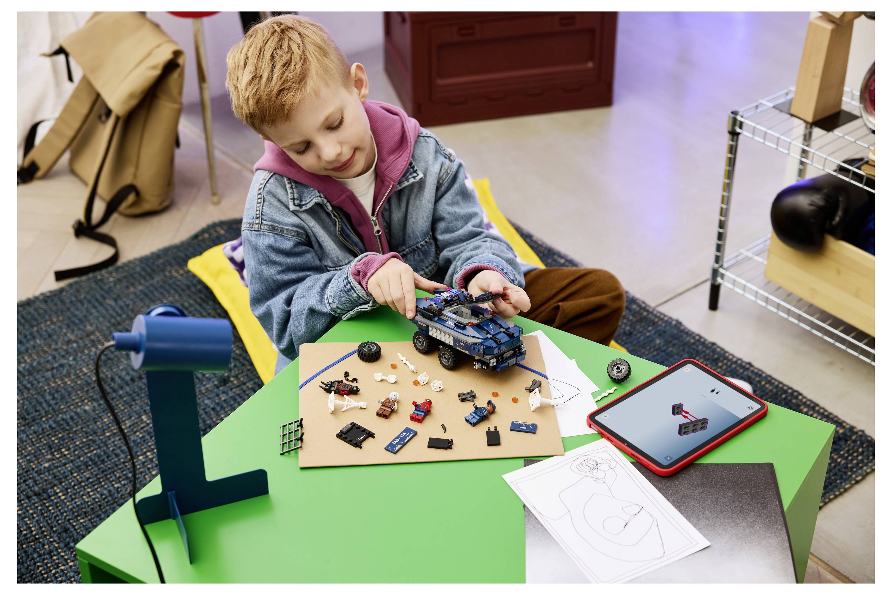 Mladý chlapec skládá hračku autíčka s elektronickými součástkami u nízího zeleného stolu, vedle něj leží tablet a instrukce.