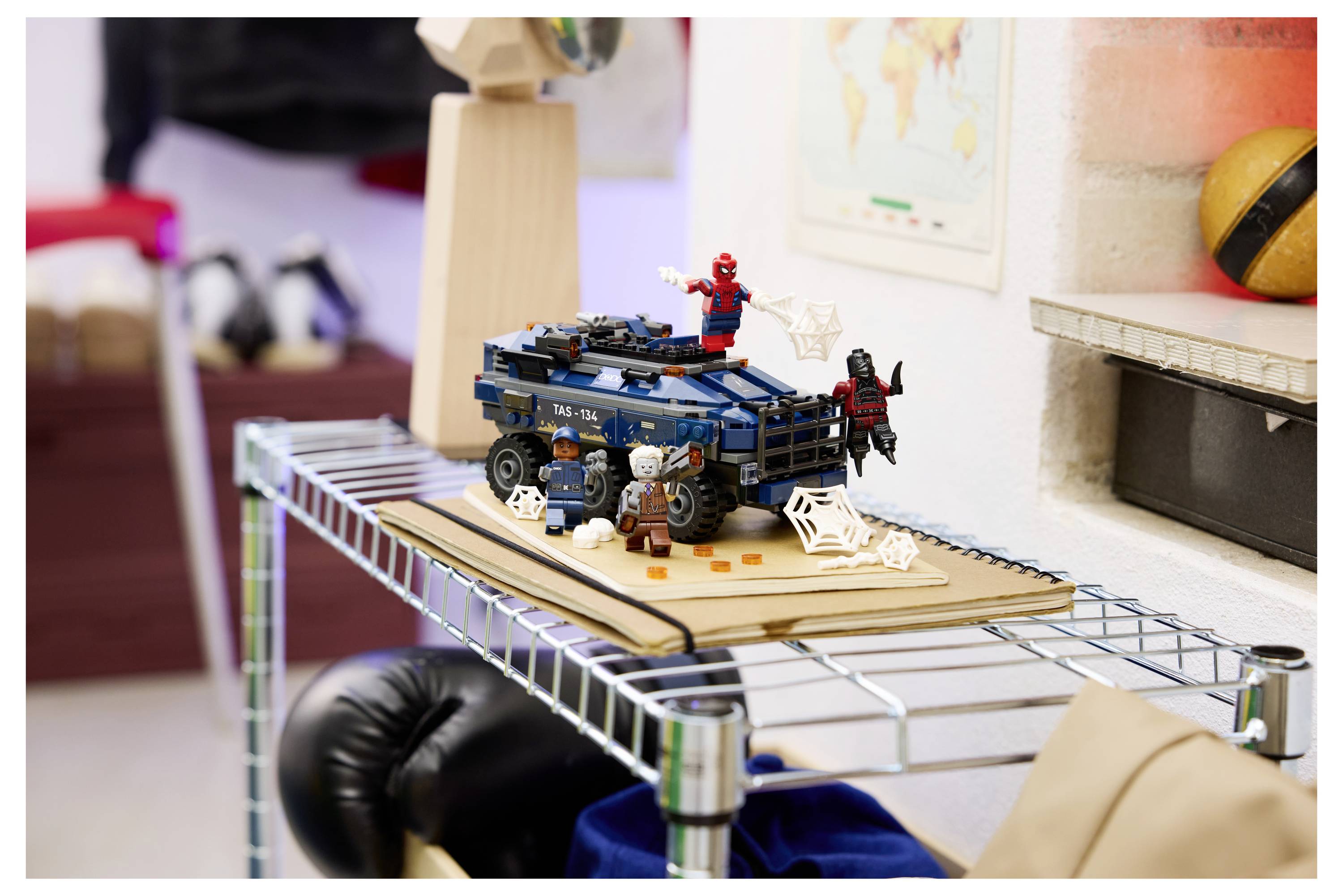 Scéna vozidla LEGO superhrdiny na polici s figurkou Spider-Mana a další postavou v pozici na modrém autě uprostřed dekorací pavučiny.
