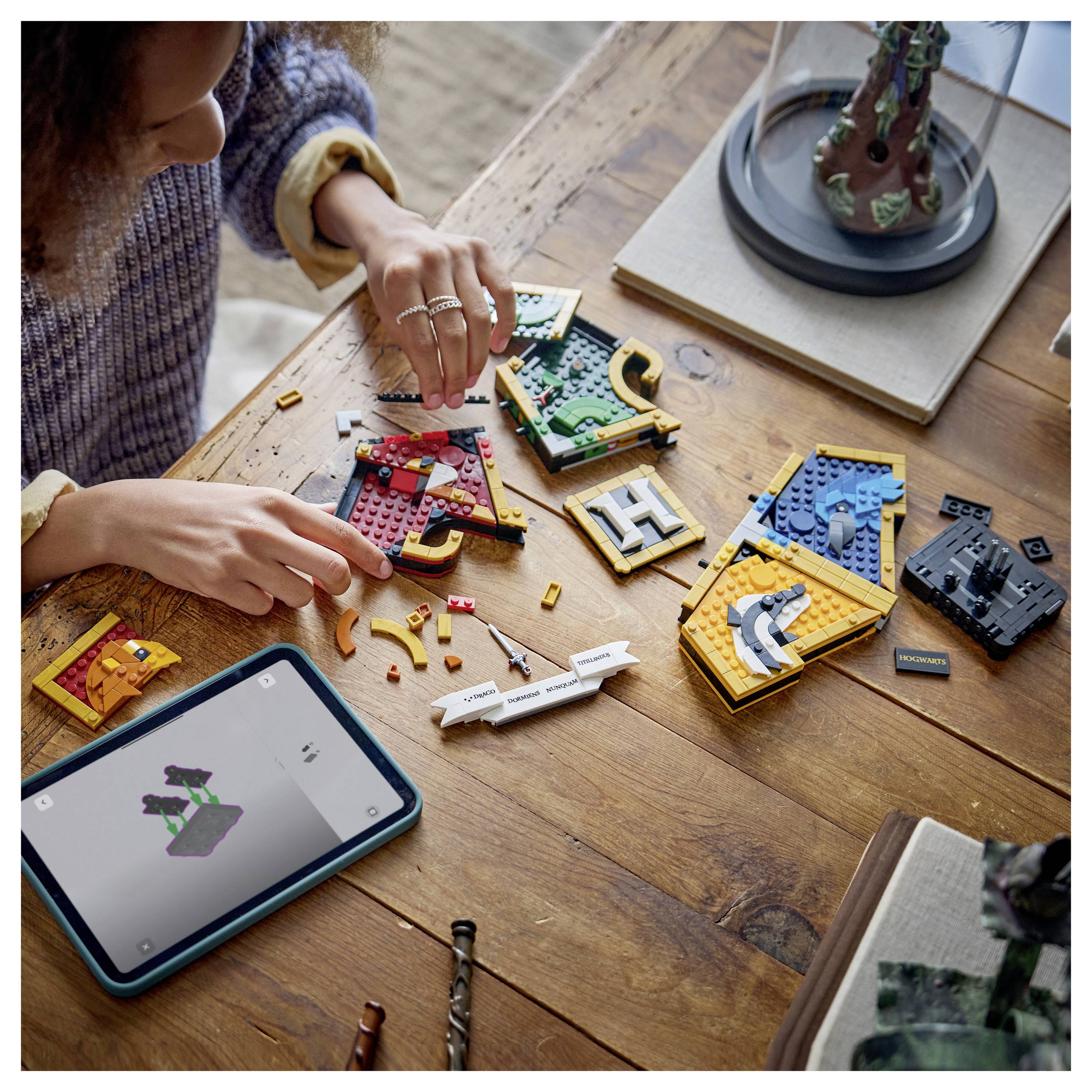 Osoba skládá stavebnice podobné LEGO dlaždice s písmeny na dřevěném stole, přičemž tablet zobrazuje pokyny pro stavbu.