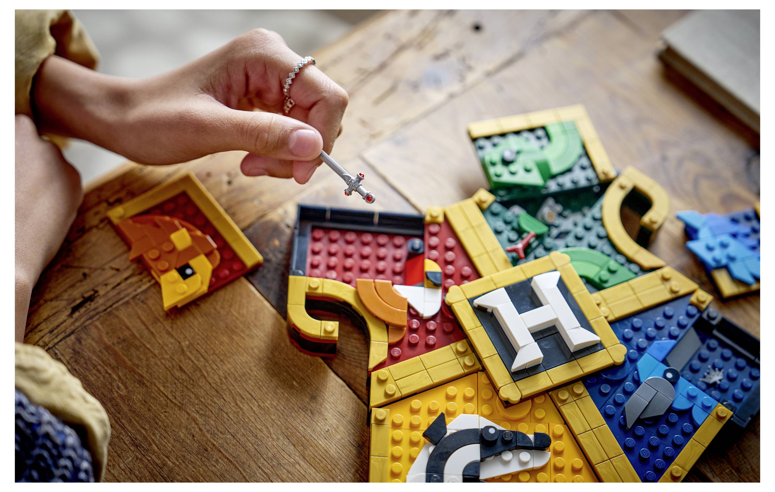 Dítě používající malý nástroj k sestavování barevného puzzle v sytlu LEGO na dřevěném stole, s propletenými díly tvořícími velký abstraktní tvar.
