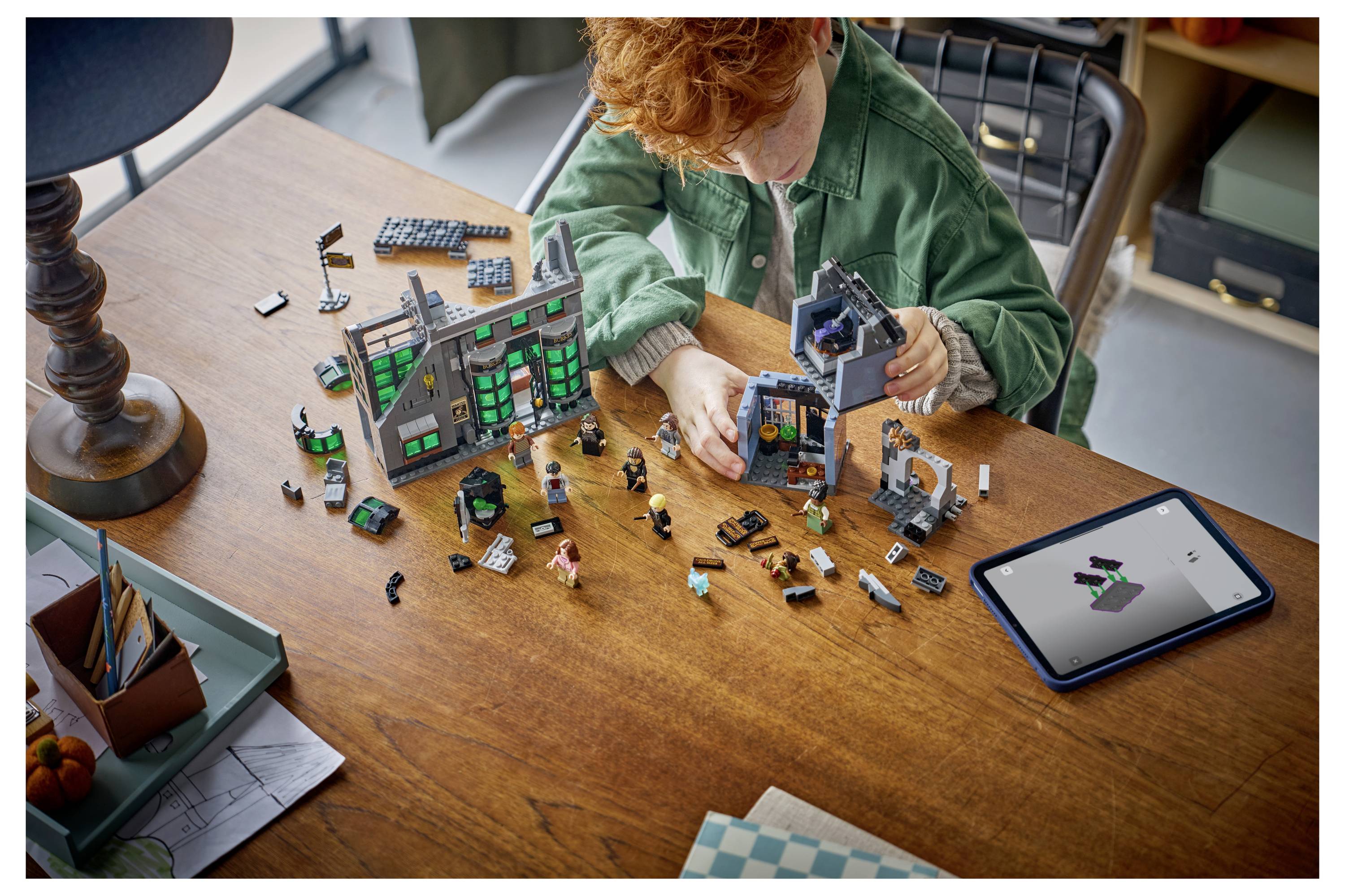 Dítě buduje LEGO dům a oblouk na dřevěném stole, vedle něj je tablet ukazující model v pokynech.