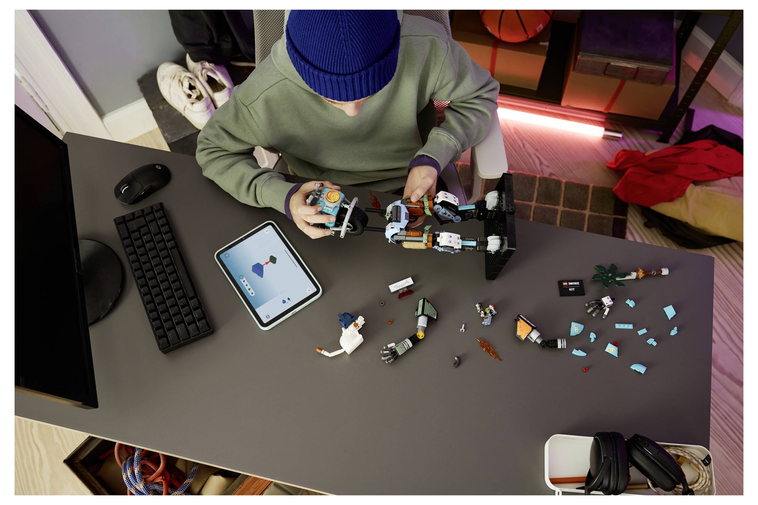 Osoba staví robota v podobě LEGO u stolu a sleduje návod na tabletu, kolem ní jsou rozptýlené součástky.