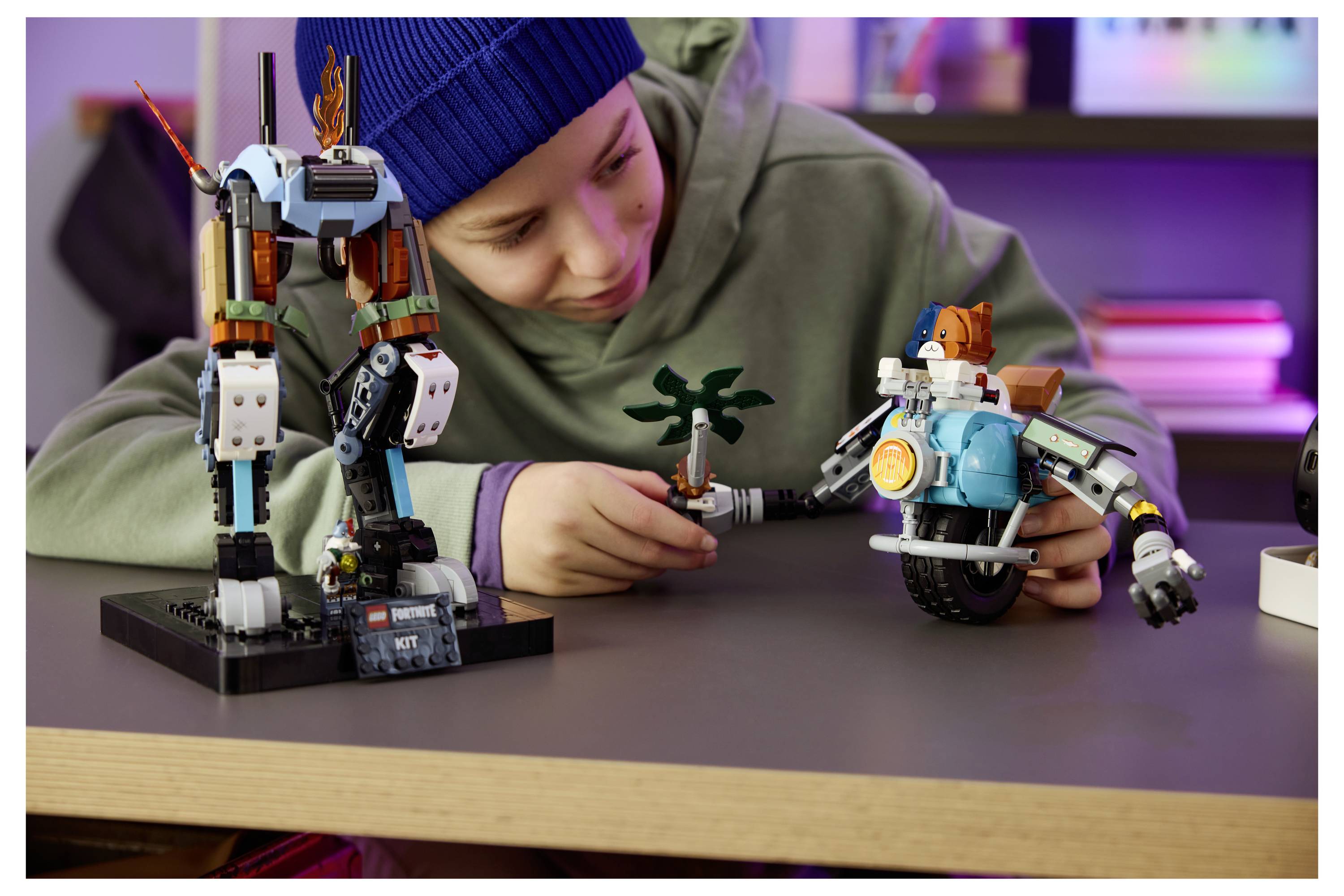 Dítě v modré čepici si hraje se dvěma robotickými hračkami a malou palmou na stole a buduje sci-fi scénu.
