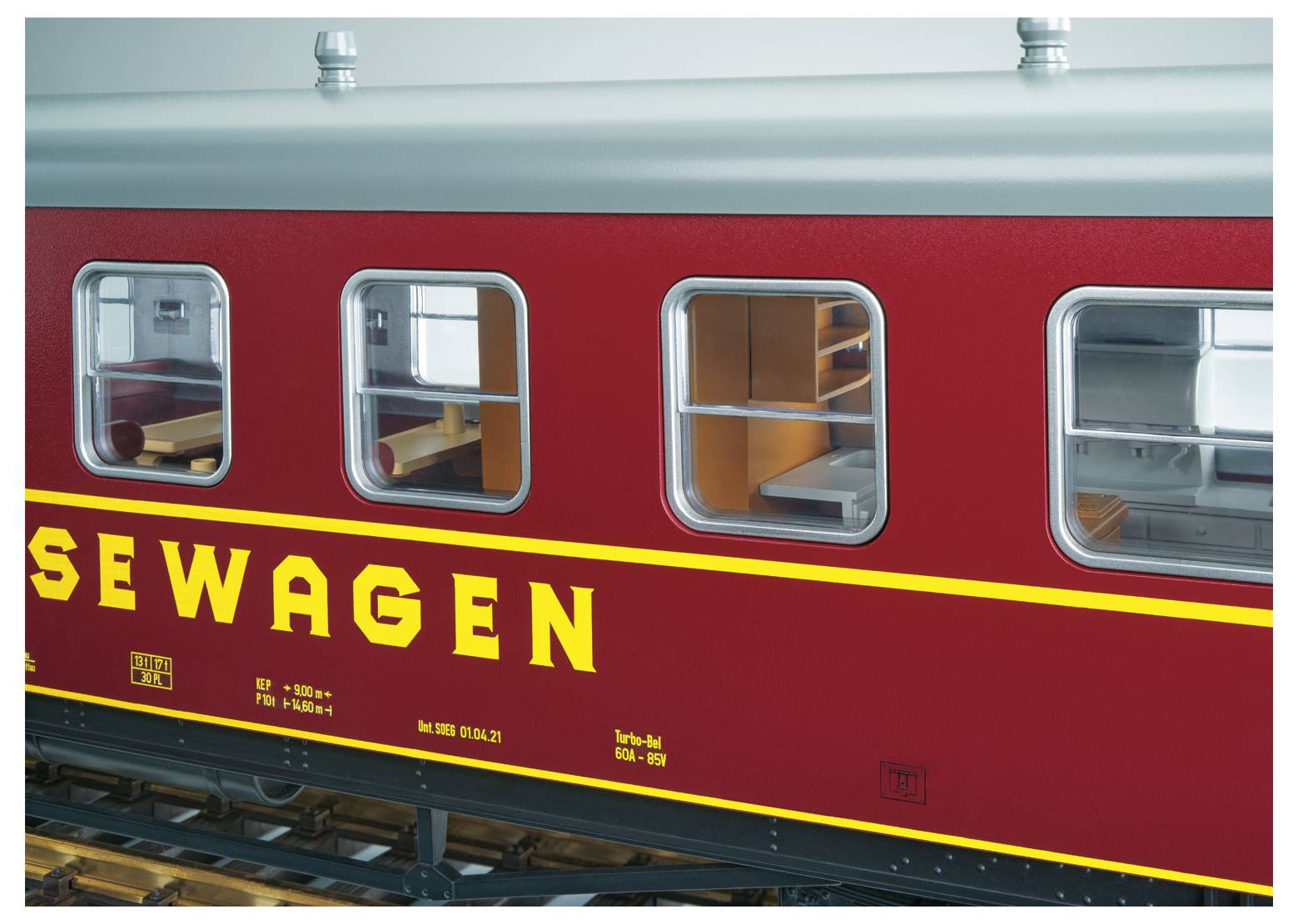 Červený vůz vlaku s okny a žlutým nápisem "SEWAGEN", zobrazený z boku v prostředí stanice nebo výstavního prostoru.