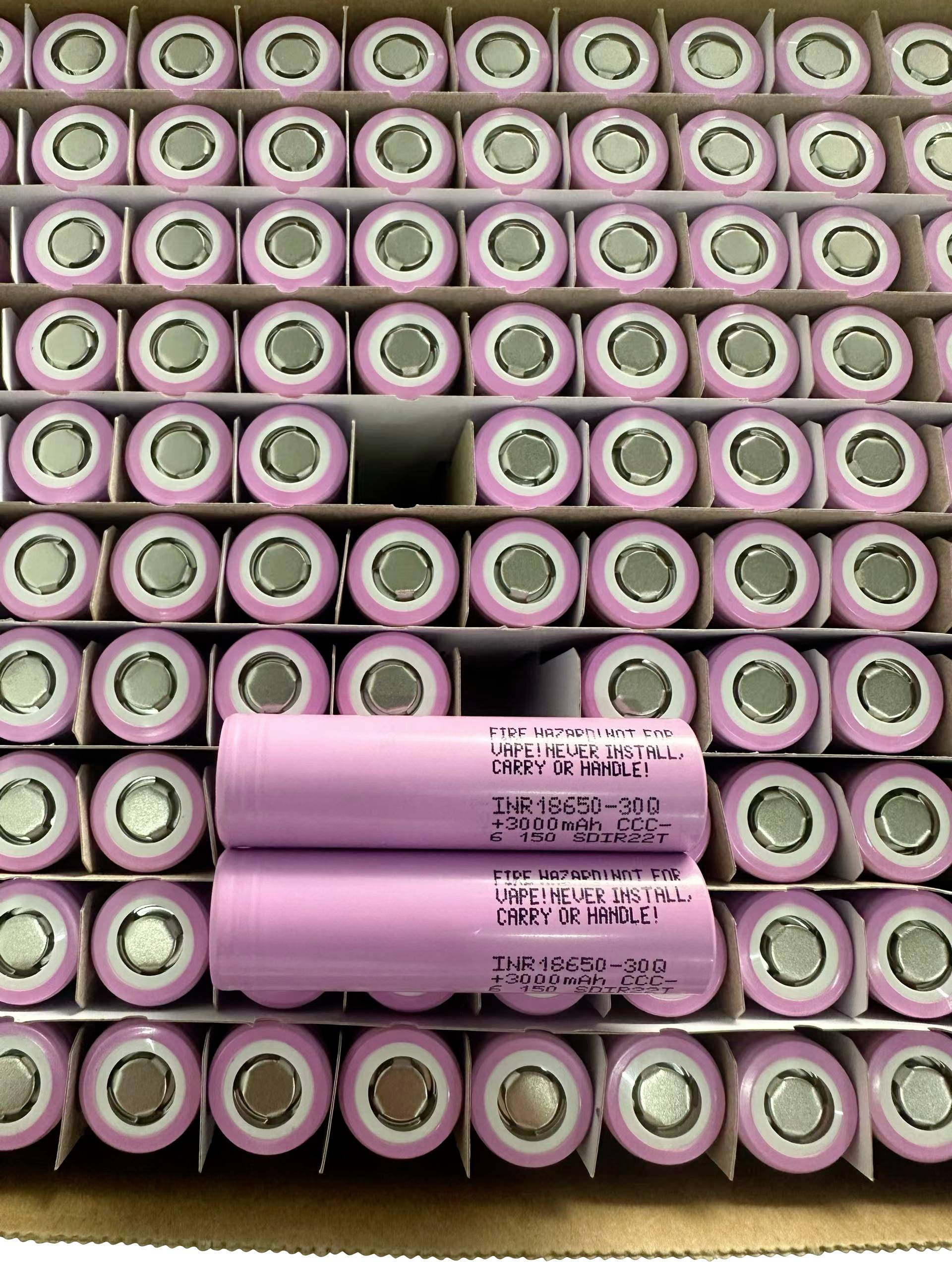 Hromada růžových válcovitých lithium-iontových baterií s dvěma buňkami označenými „INR18650-30Q" ležícími přes střed.