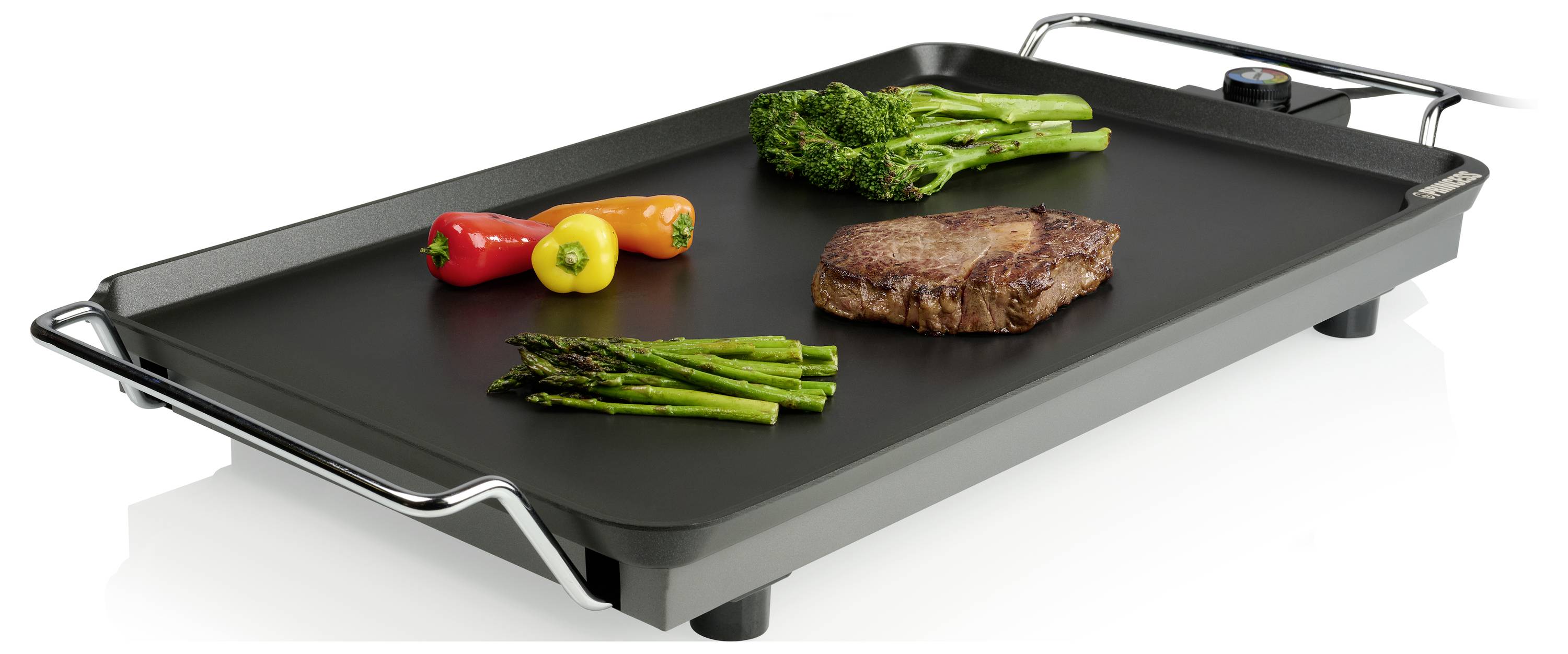 Elektrický stolní grilovací plát se steak, chřestem, brokolicí a paprikou vaří na jeho černém plochém povrchu.