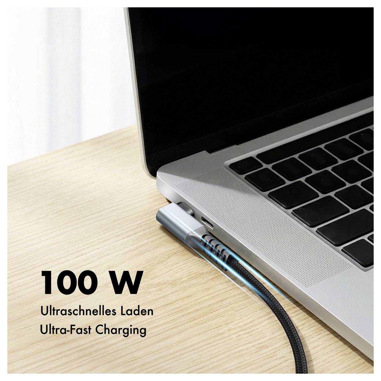 Notebook připojený k nabíjecímu kabelu na stole s textem "100 W", "Ultraschnelles Laden" a "Ultra-Fast Charging".