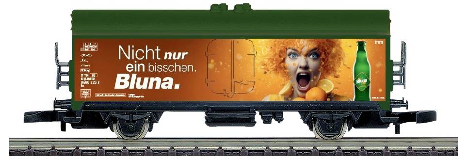 Zelený nákladní vagon vlaku s oranžovou reklamou Bluna zobrazující křičící ženu a sloganem "Nicht nur ein bisschen. Bluna."