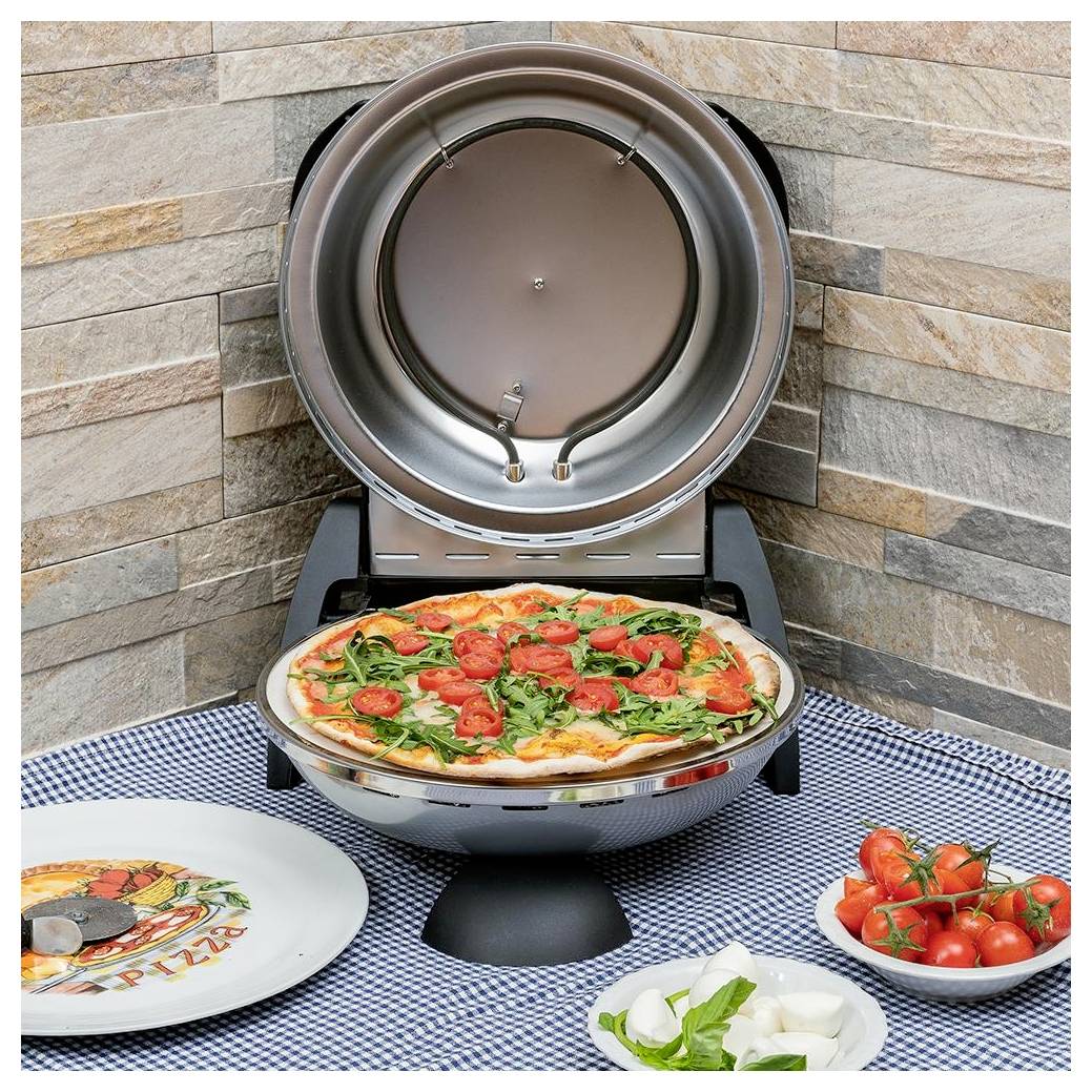 Venkovní kuchyňská linka s pizzovou pecí, ve které se péče pizza, obklopená talíři a mísami čerstvých ingrediencí na kostkovaném ubru.