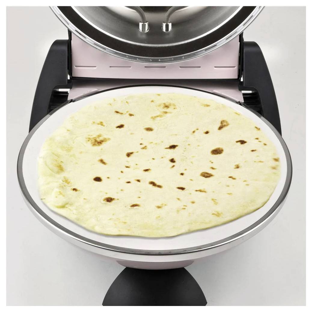 Plochá tortilla leží na kulaté elektrické desce, s otevřeným víkem nahoře, což naznačuje, že se vaří nebo ohřívá.