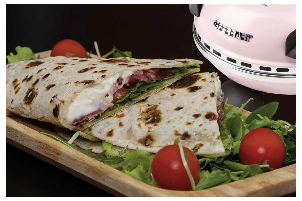 Grilovaný skládaný chlebový sendvič na dřevěné desce s cherry rajčaty a zeleninou, vedle růžového tiskacího lisu na sendviče.