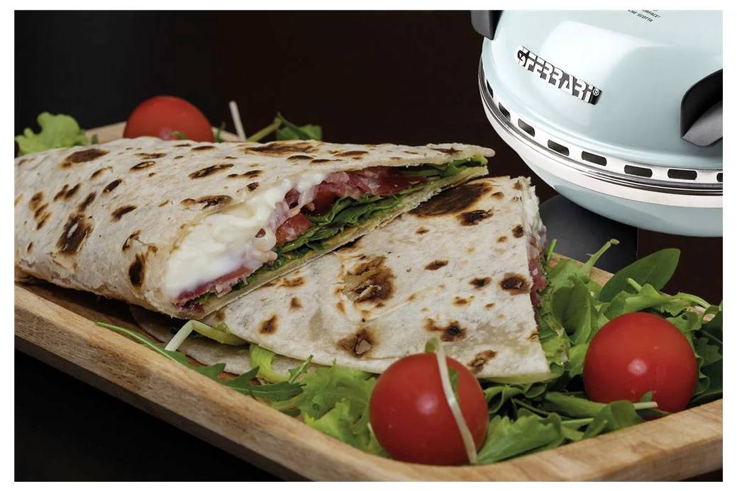 Grilovaný wrap sendvič na dřevěné desce s hlávkovým salátem a cherry rajčaty, vedle světle modrého sendvičovače.