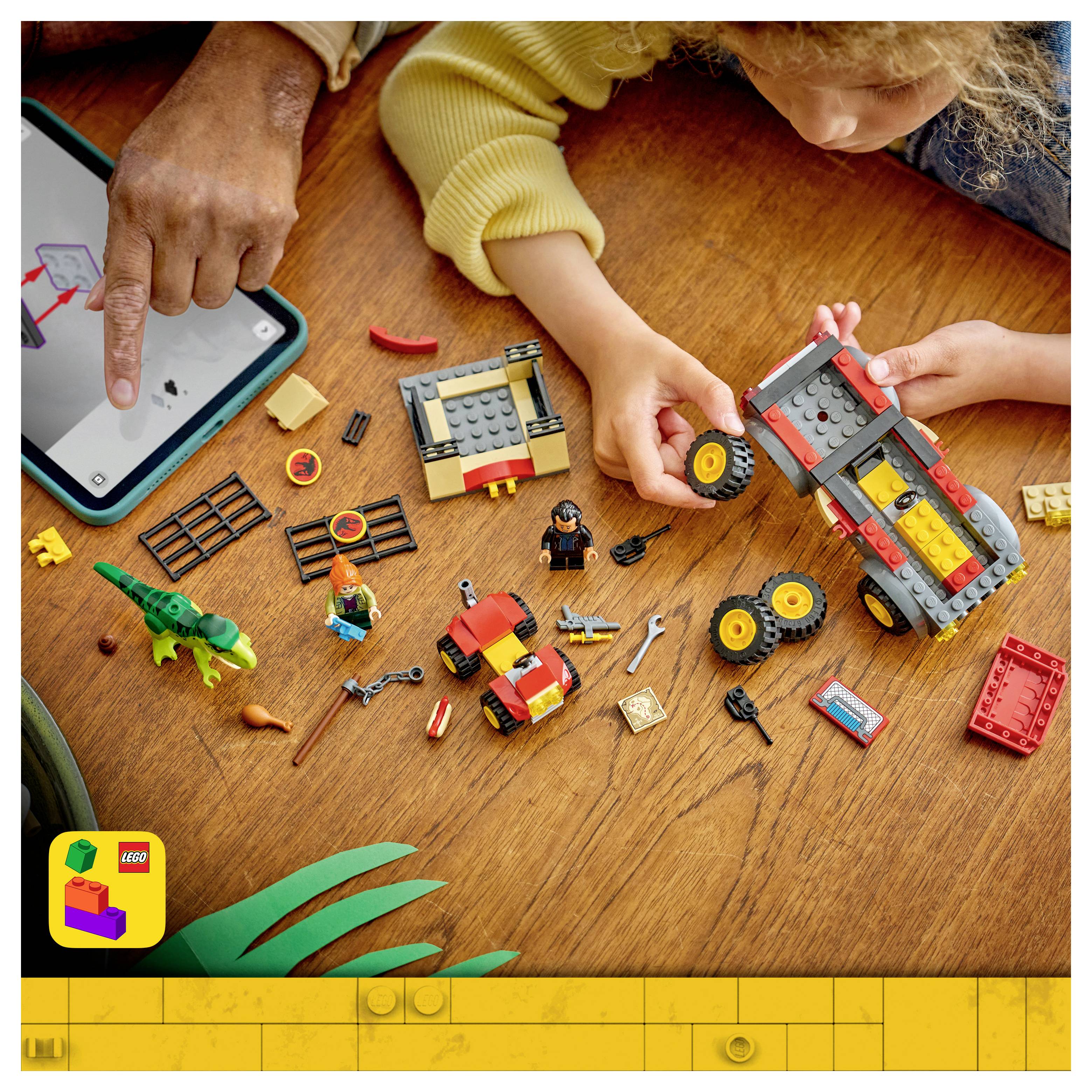 Dítě a dospělý staví LEGO vozidlo na dřevěném stole a zároveň používají tablet s pokyny; v blízkosti jsou rozesety LEGO díly a figurky.
