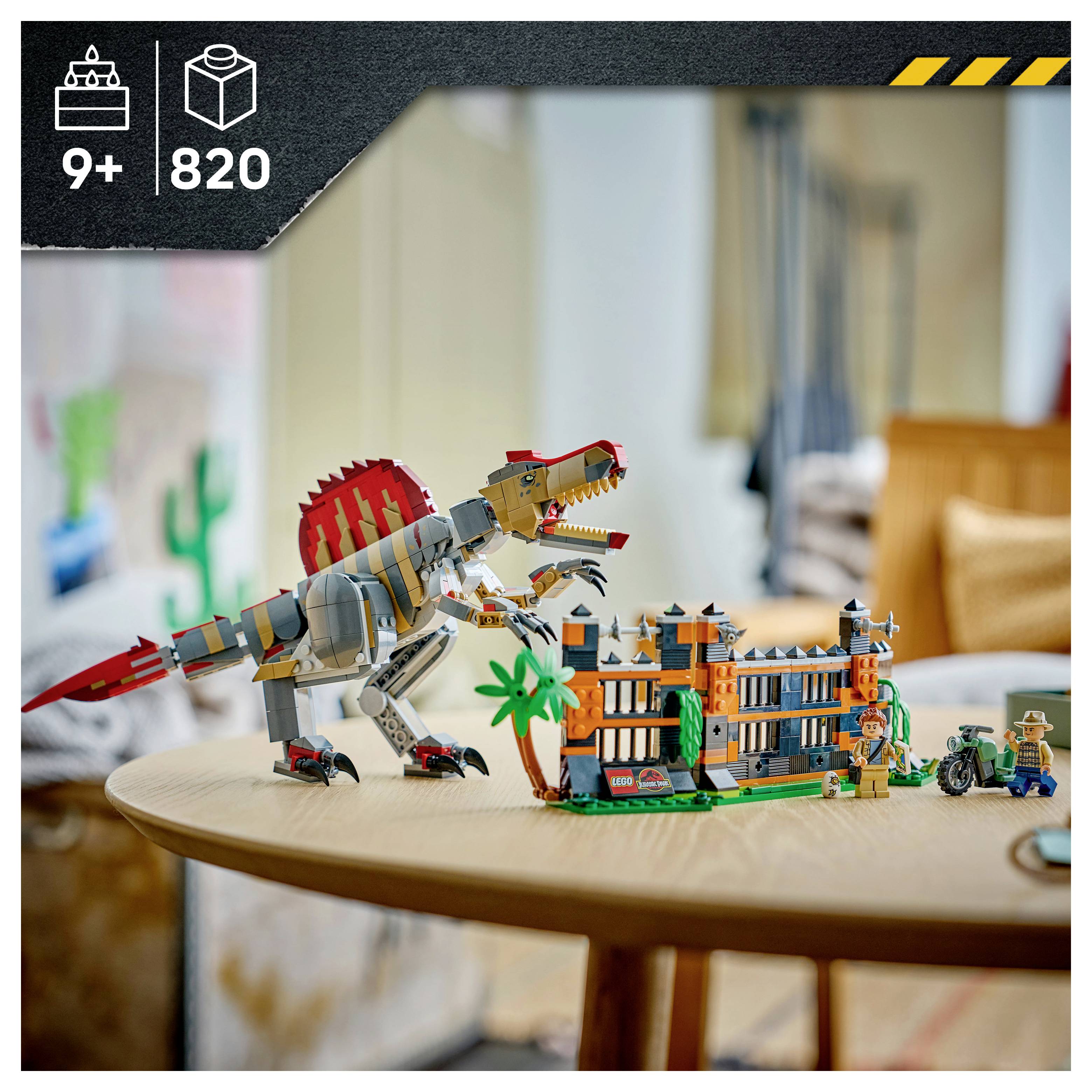 LEGO sada dinosaura na stole, s T. rexem vedle vícepatrové budovy a minifigurkami; obal zobrazuje věk 9+ a 820 dílků.
