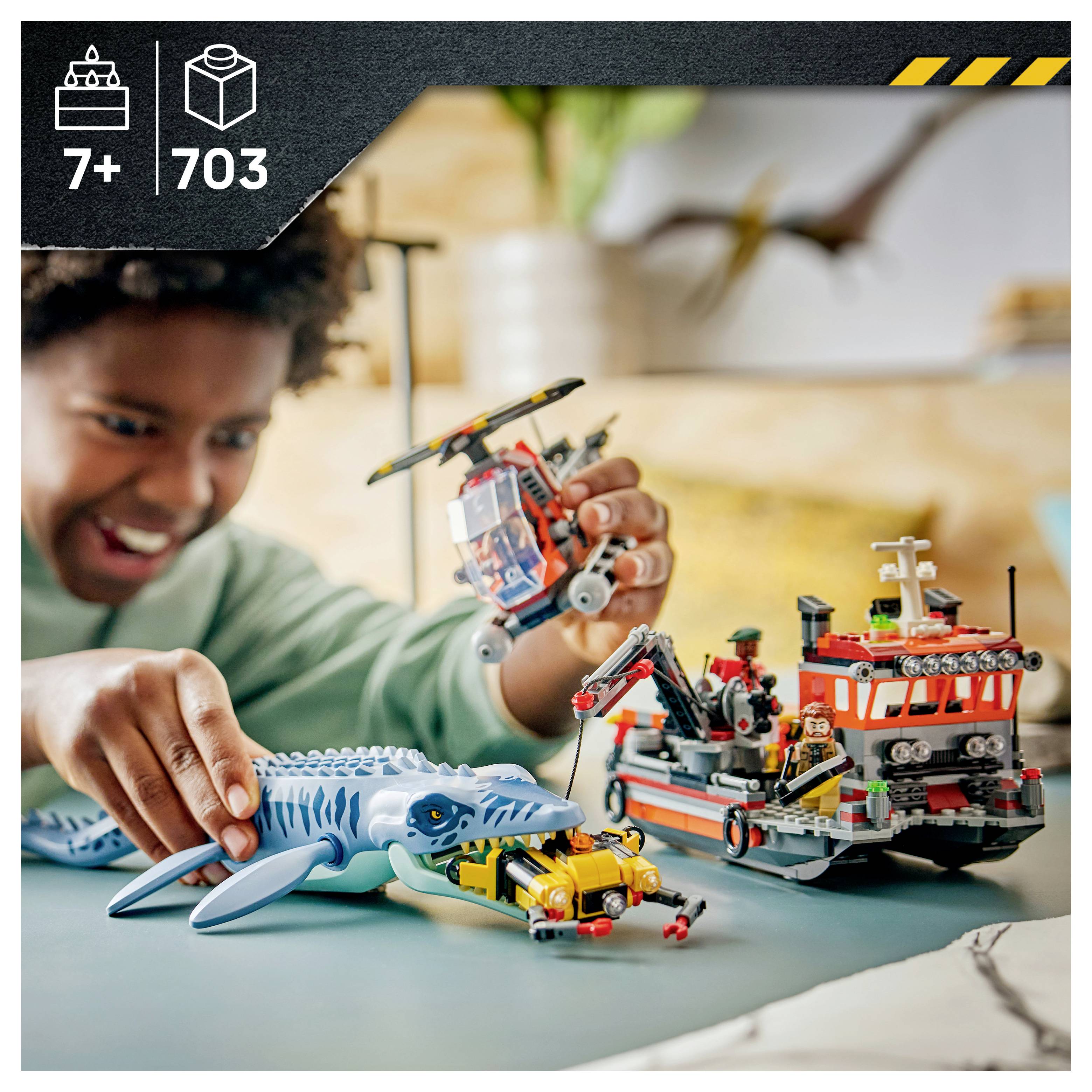 Dítě si hraje s hračkami na záchranu v oceánu ve stylu LEGO, včetně žraloka, helikoptéry a záchranného člunu. Sada je označena pro věk 7+ a obsahuje 703 dílků.