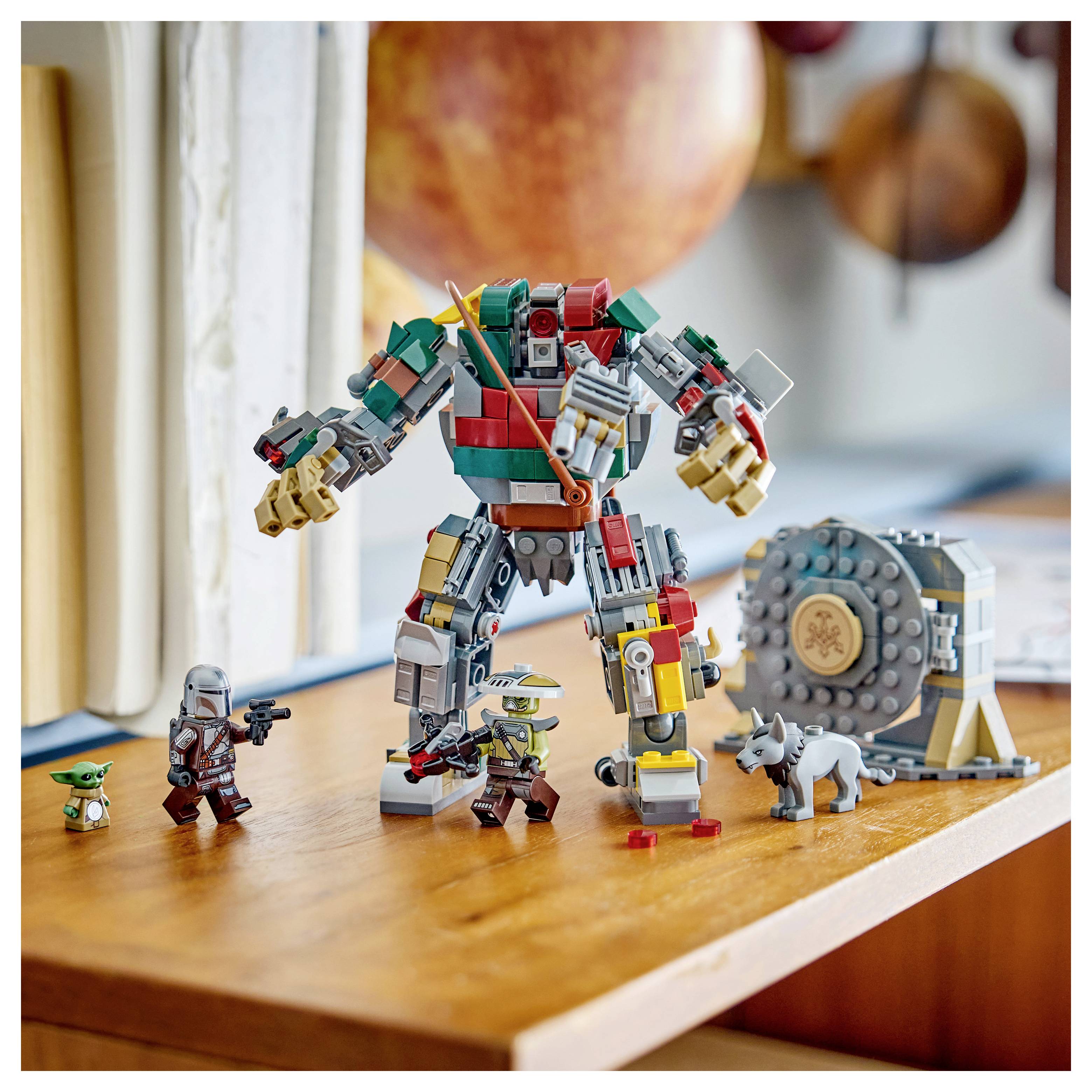 LEGO-postavička robota ve stylu LEGO stojící na dřevěném stole s několika malými minifigurkami a stavebnicovým kolem kolem ní.