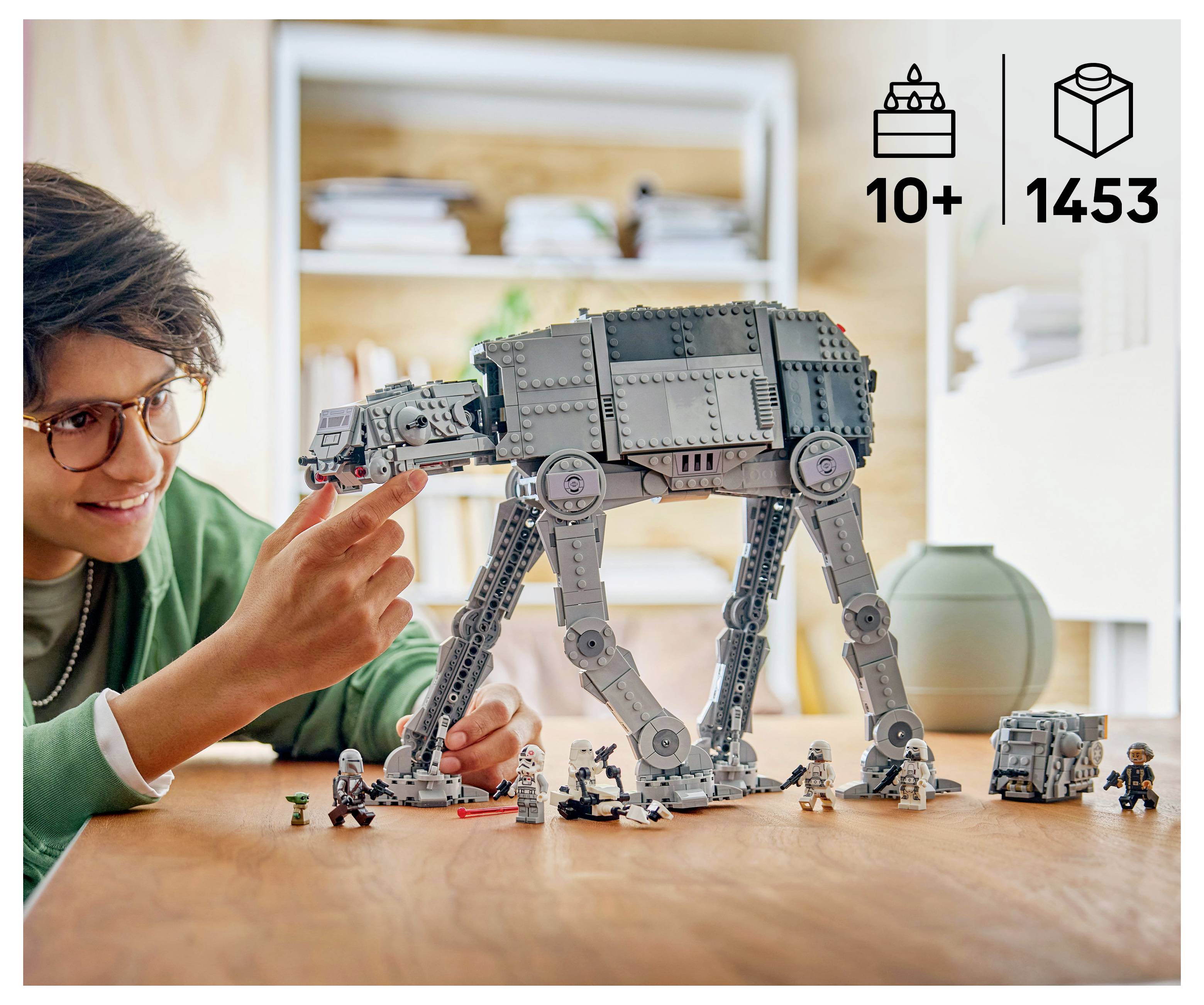 Osoba skládající LEGO model AT-AT chodce na stole s ikonami produktu '10+' a '1453' v rohu.