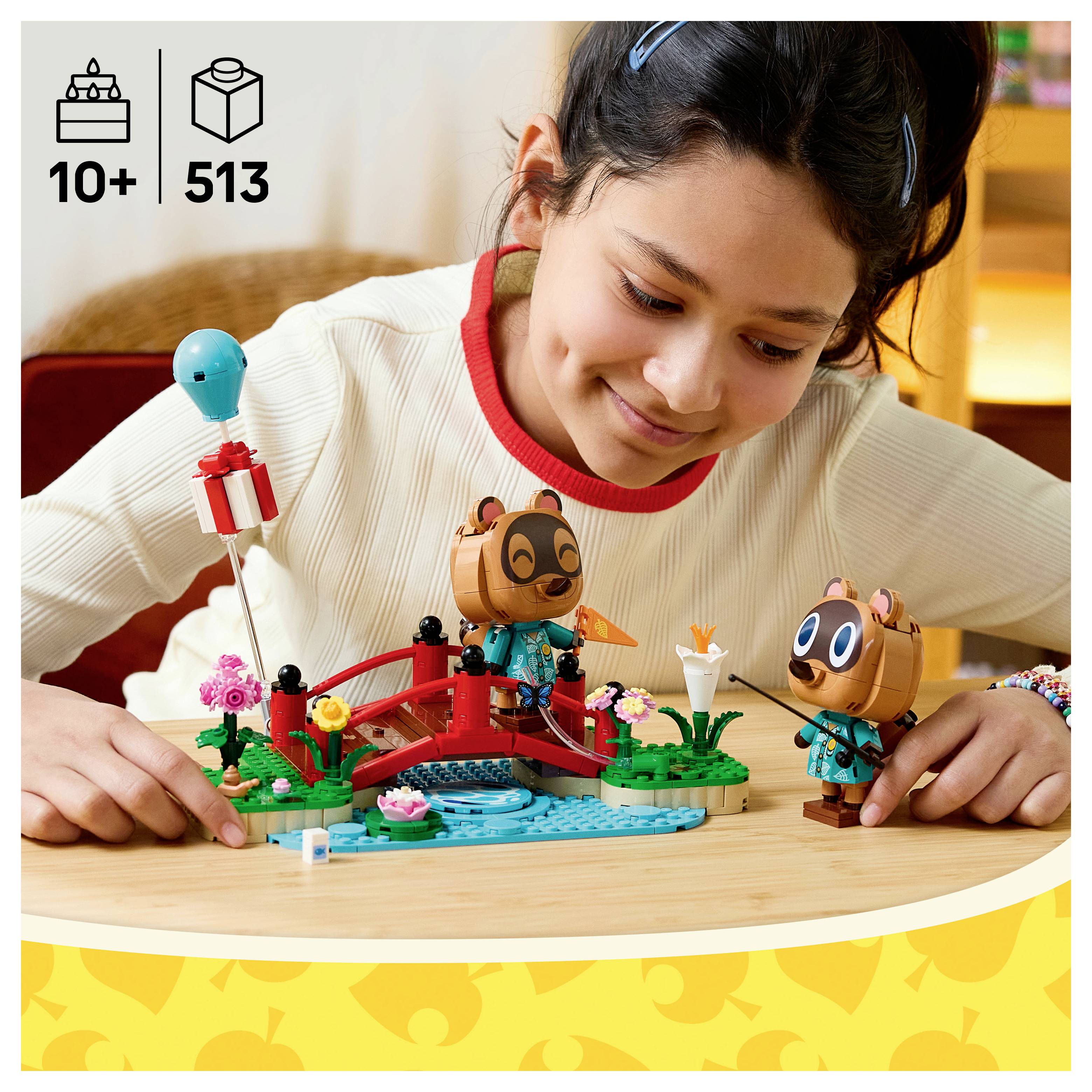 Dívka si hraje se stavebnicí zvířat ve stylu LEGO na stole s ikonami "10+" a "513" pro věk a počet dílků v levém horním rohu.