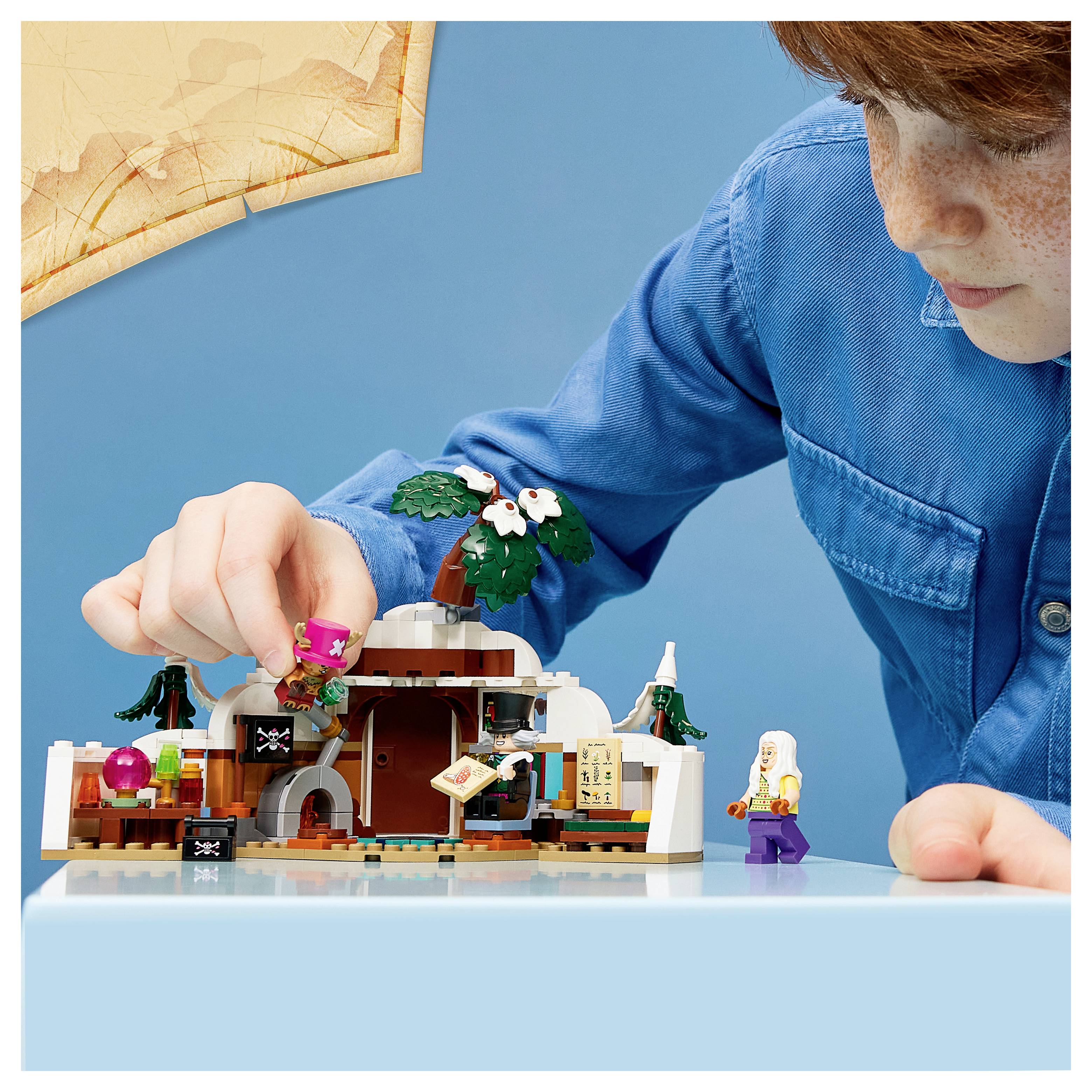 Dítě si hraje s vytvářením pevnosti na ostrově ve stylu LEGO na stole, umísťuje figurku blízko malé tropické scény s palmou a minifigurkami.