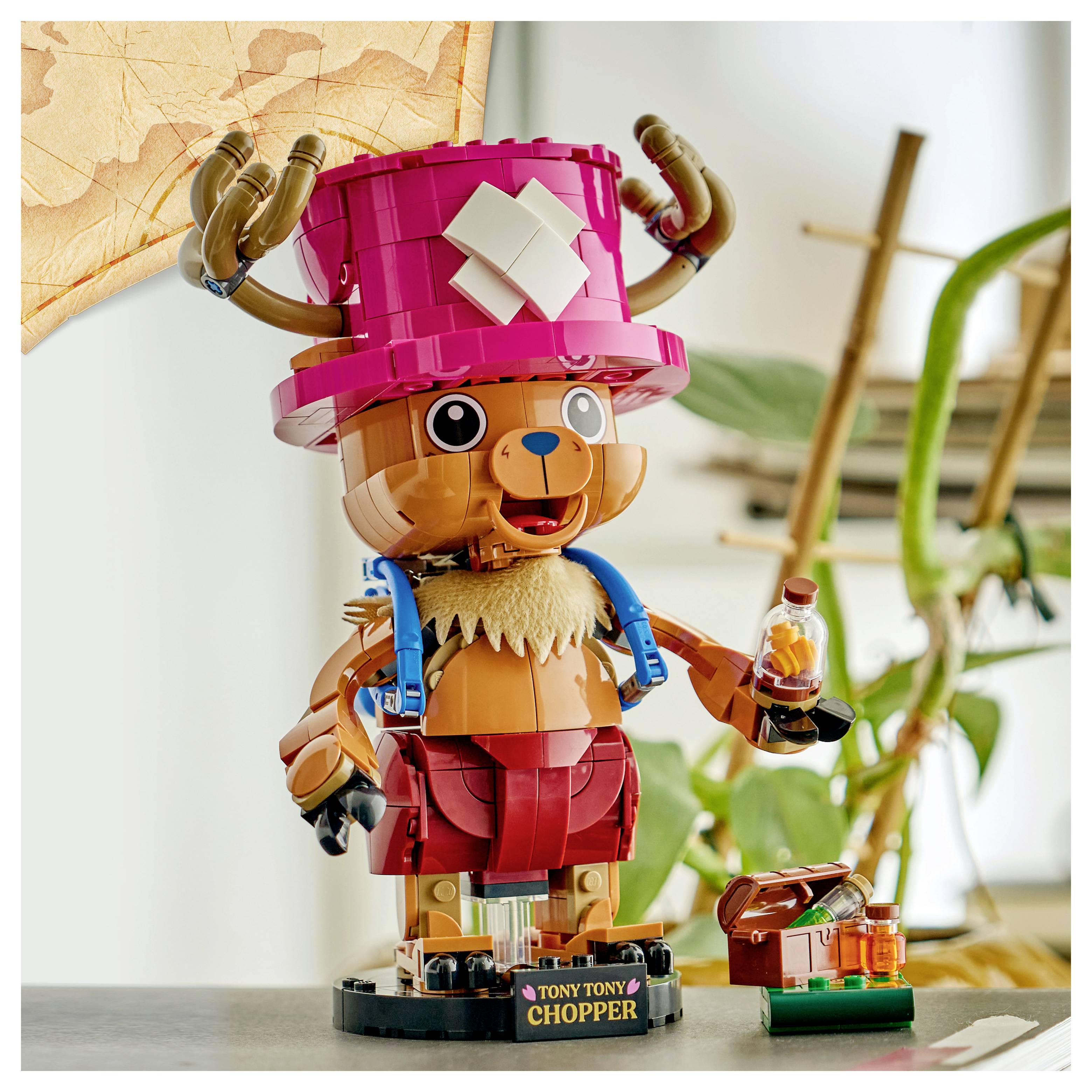 LEGO figurka Tony Tony Choppera v růžovém klobouku a červených šortkách, stojící na podstavci s displeje a držící lahev, s malou částí příslušenství vedle ní.