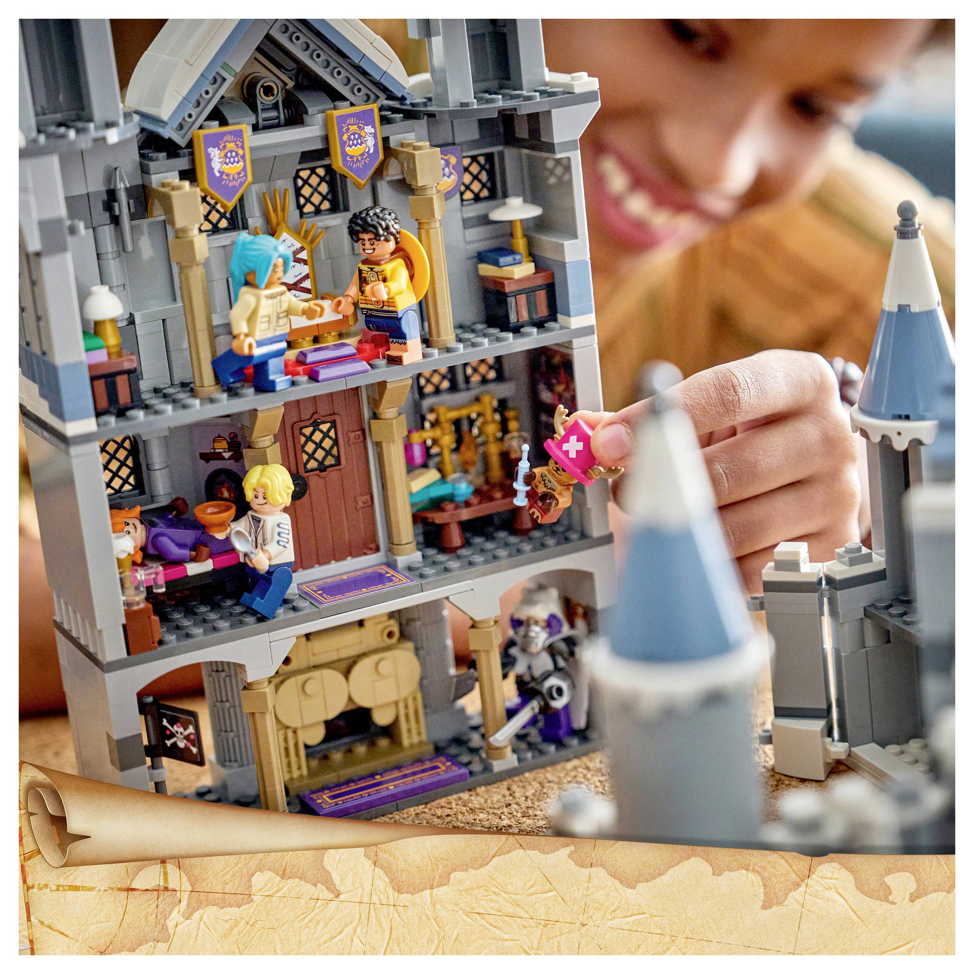 Dítě si hraje se stavebnicí typu LEGO zámku, umisťuje malou figurku do vícepatrové středověké věže s miniaturními postavičkami uvnitř.