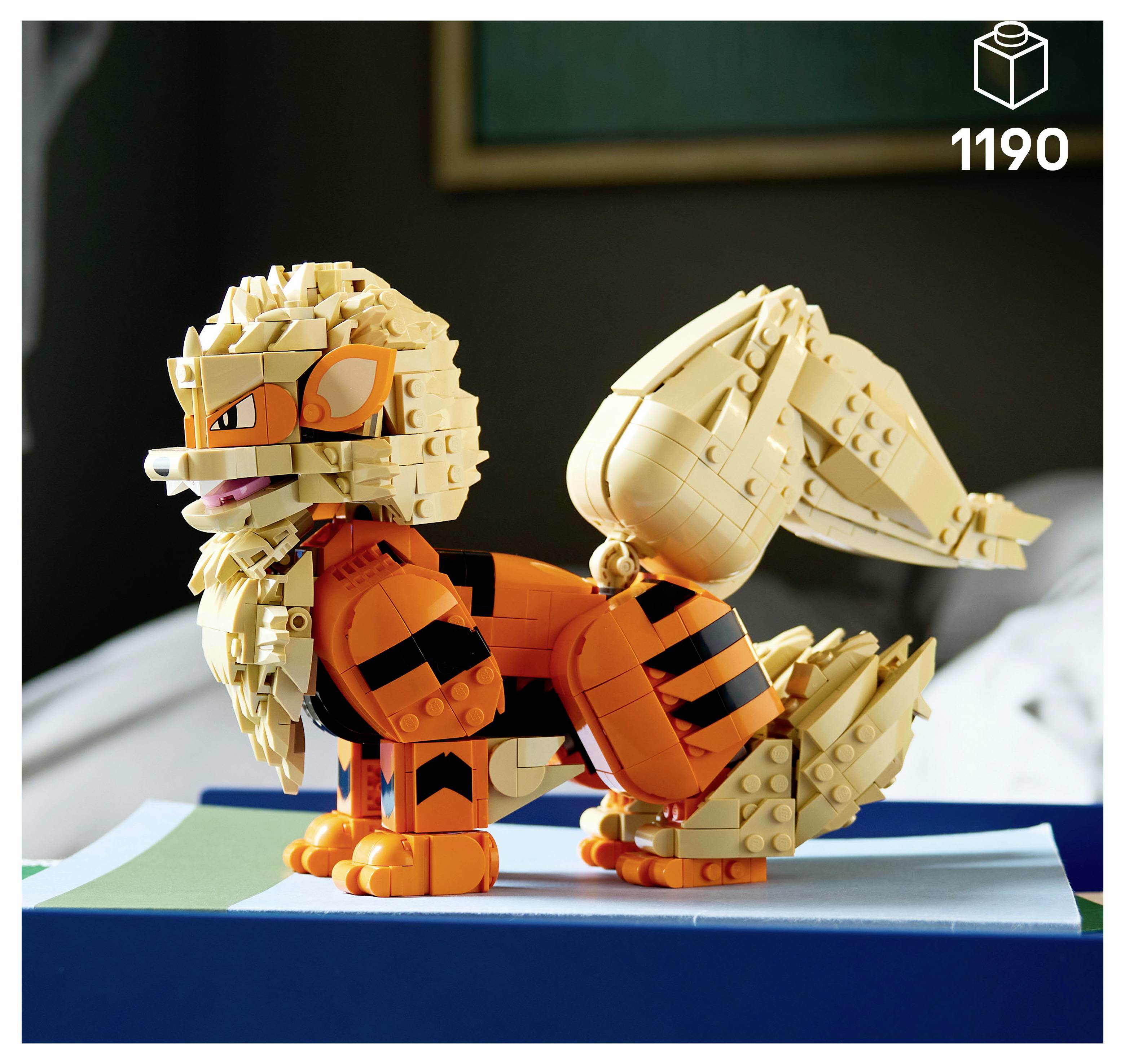 LEGO stylizovaná postava lišky postavená z oranžových a béžových kostek, umístěná na modré výstavní podstavci.