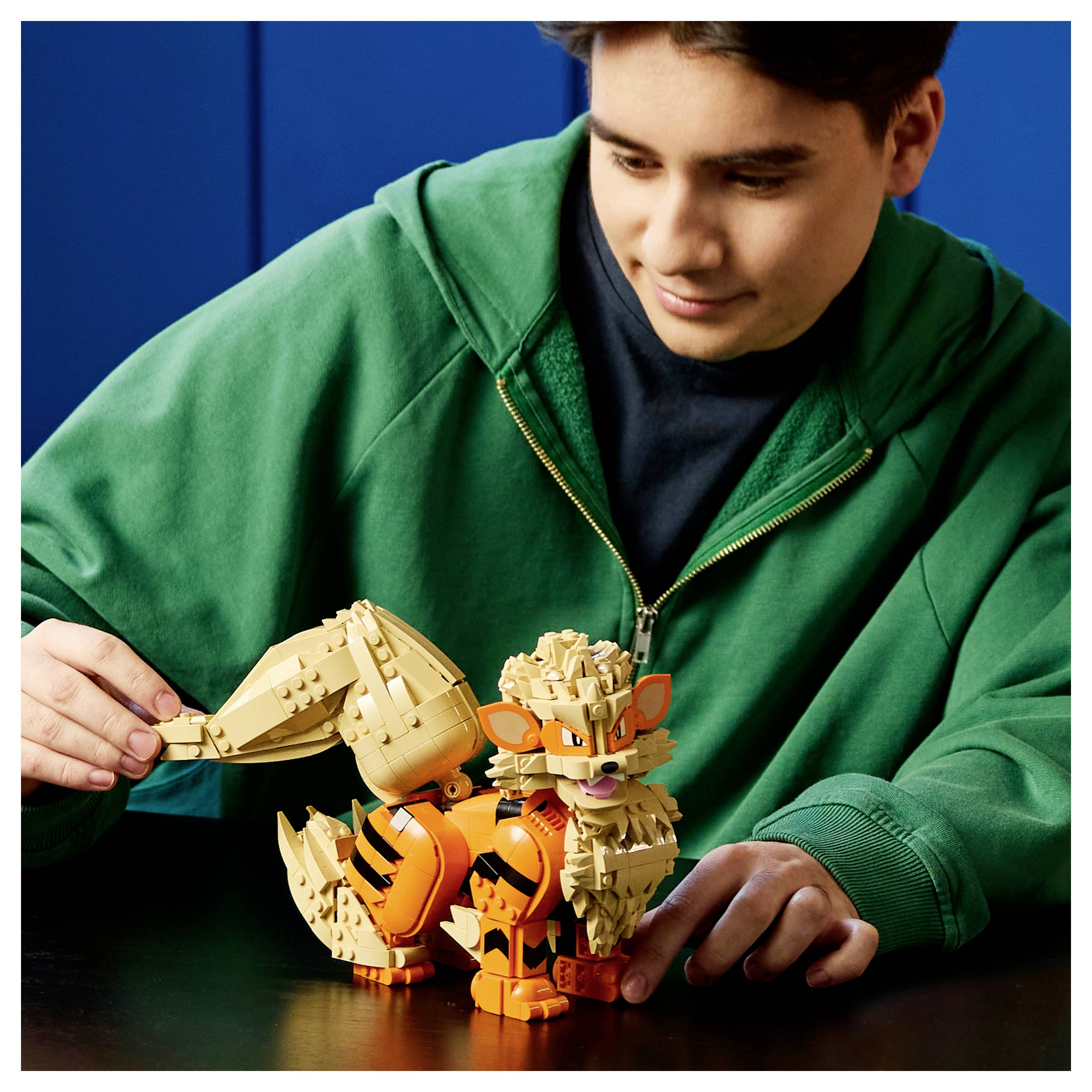 Teenager v zelené mikině skládá LEGO-style model lišky v oranžové a béžové barvě na stole.
