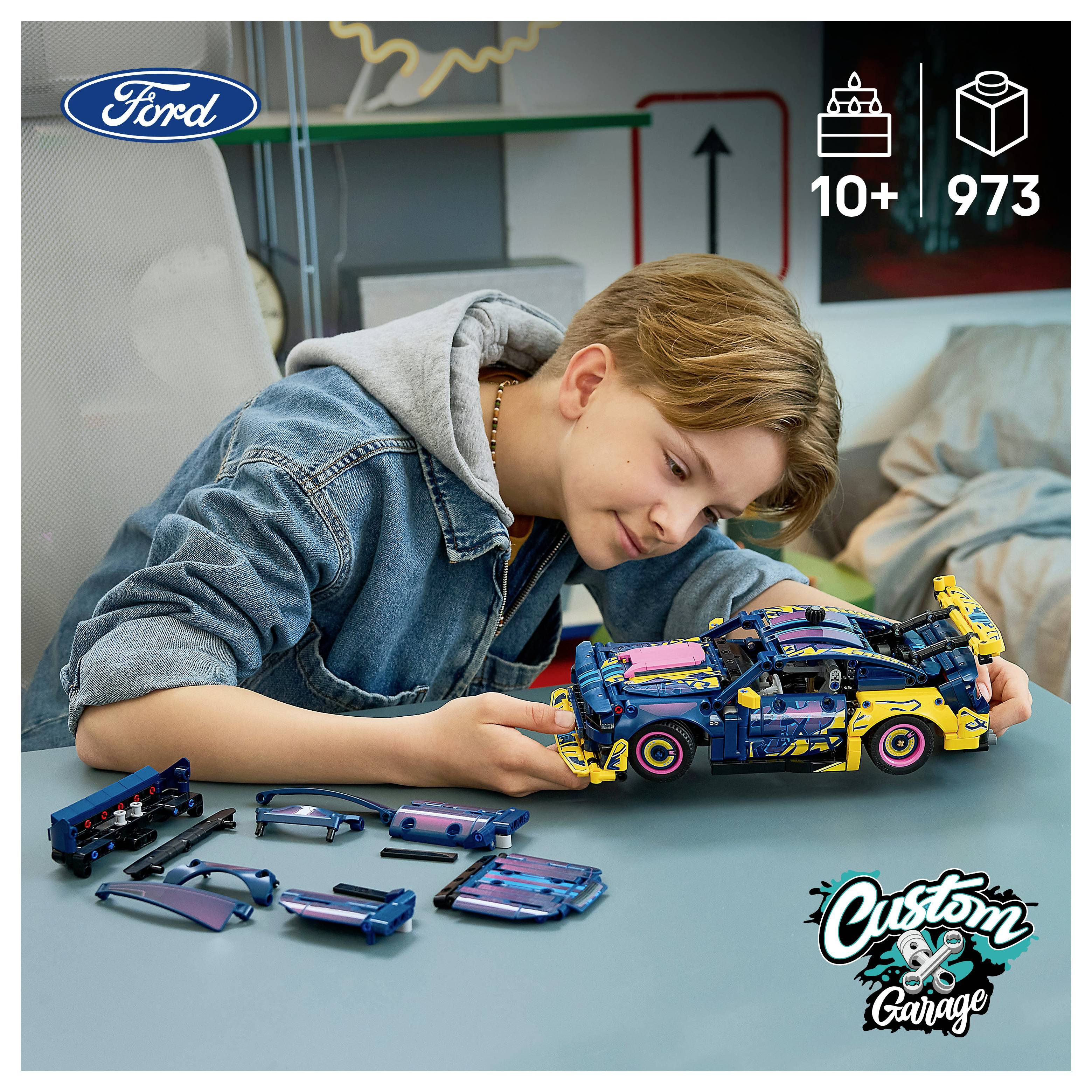 Chlapec skládá LEGO podobný model auta Ford u stolu, s rozloženými díly vedle něj a '10+' a '973' zobrazenými v rohu.