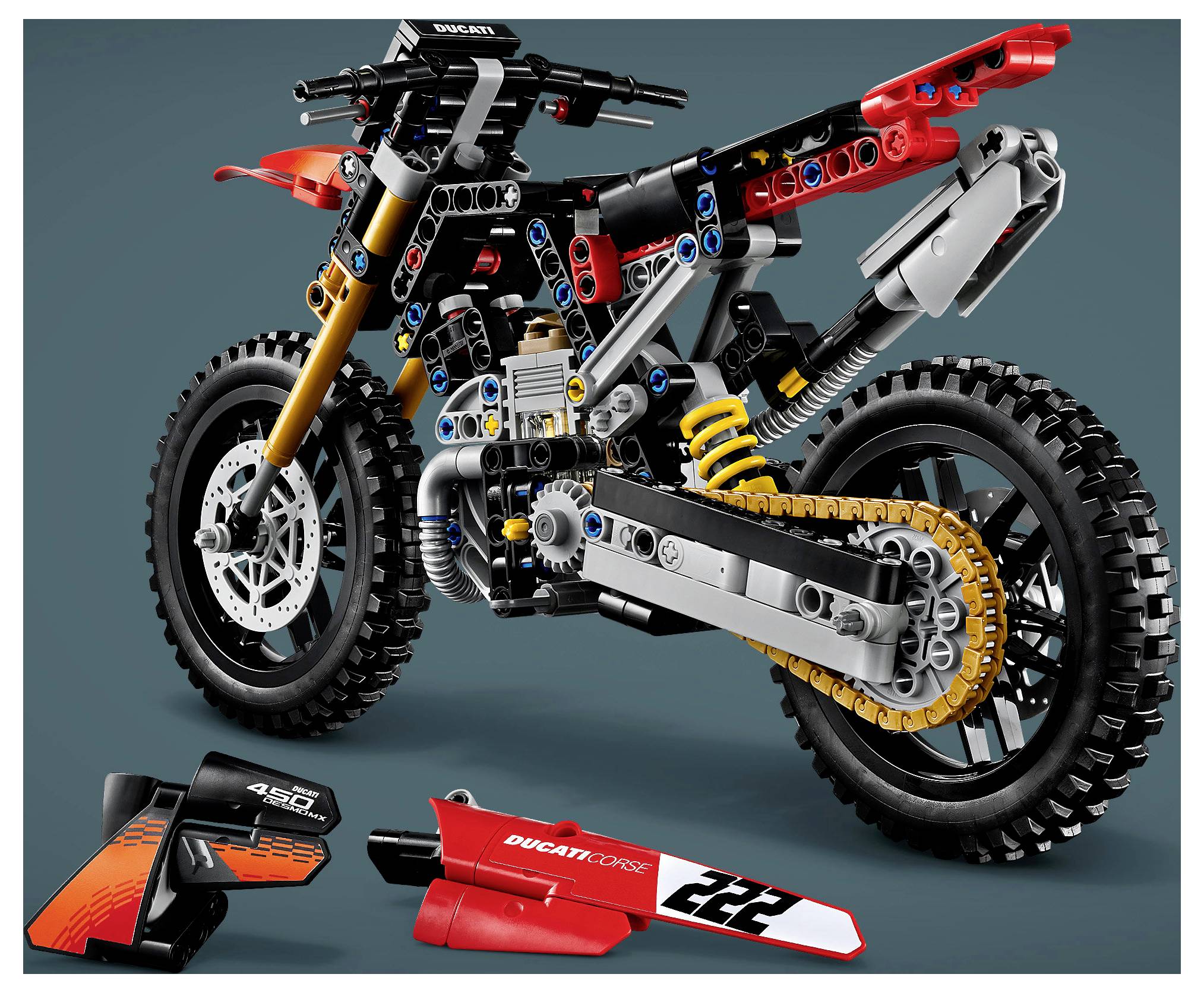 Rozložený pohled na model terénního motocyklu LEGO Ducati s odpojenými obody zobrazený níže, zvýrazňující jeho rám, odpružení, řetěz a kola.