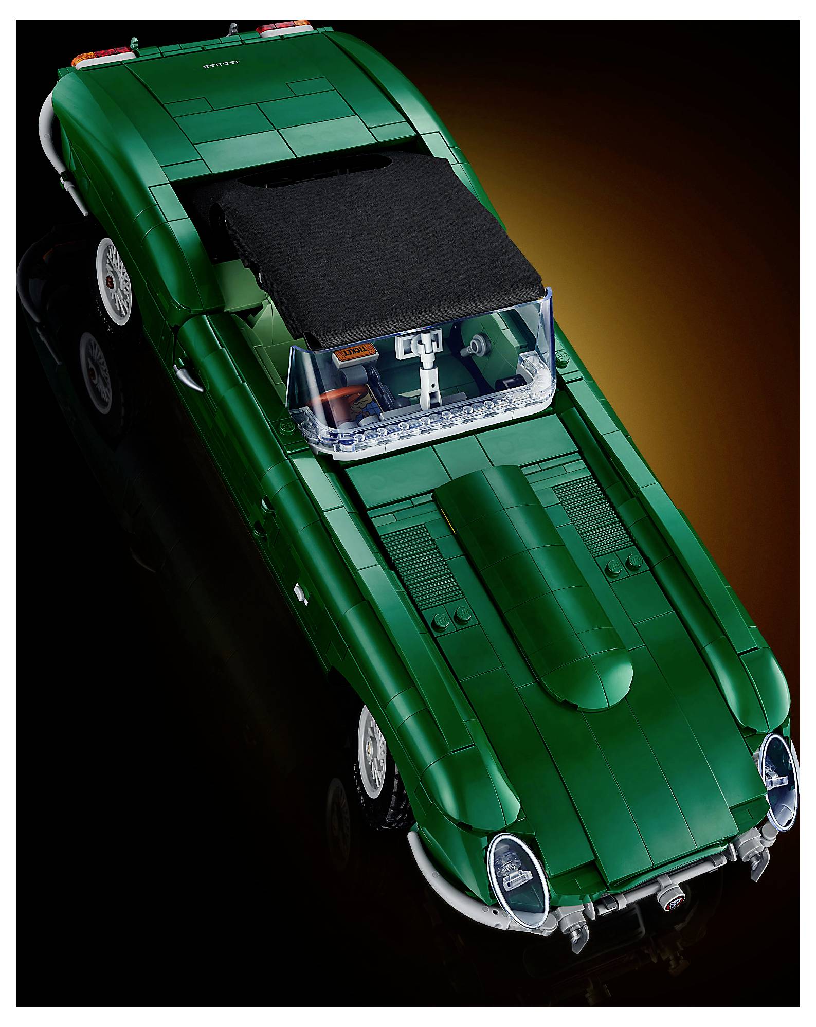 Pohled shora na zelený vintage model sportovního automobilu s černou střechou a pneumatikami s bílými stěnami na tmavém pozadí.