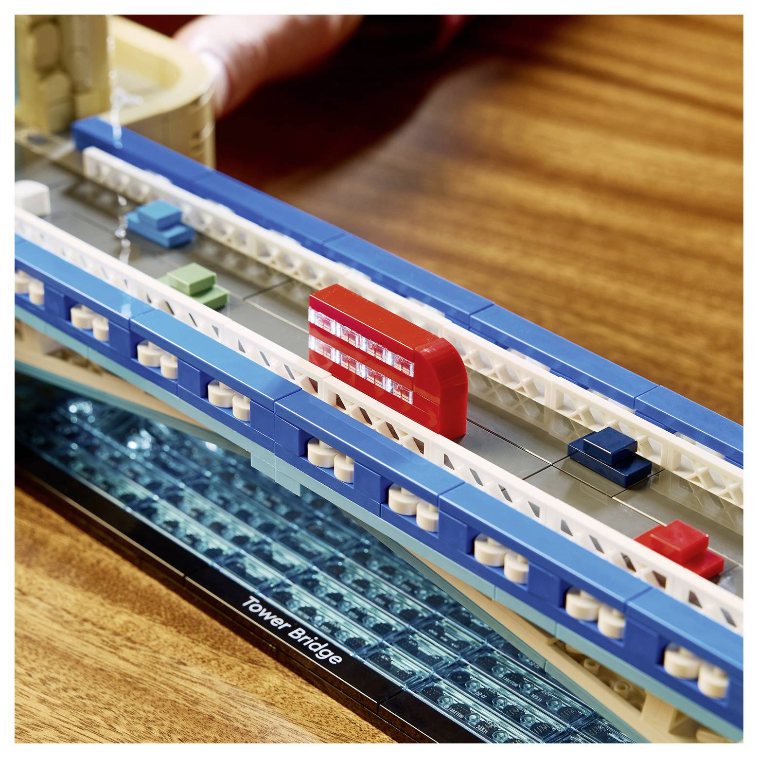 Model LEGO Tower Bridge na dřevěném stole s červeným dvoupodlažním autobusem přejíždějícím přes rozpětí mostu.