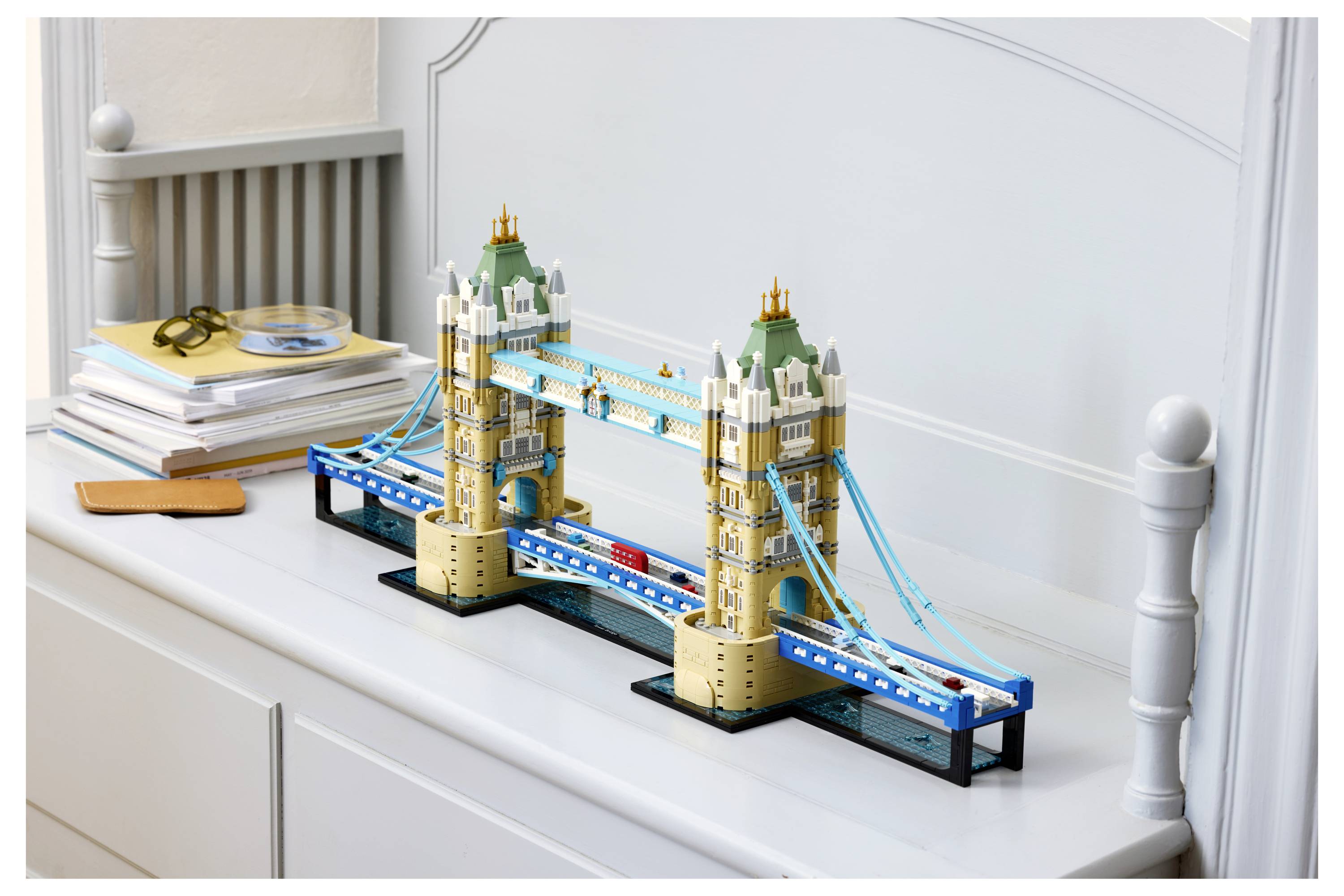 LEGO model londýnského Tower Bridge vystavený na bílé komodě vedle knih a brýlí.